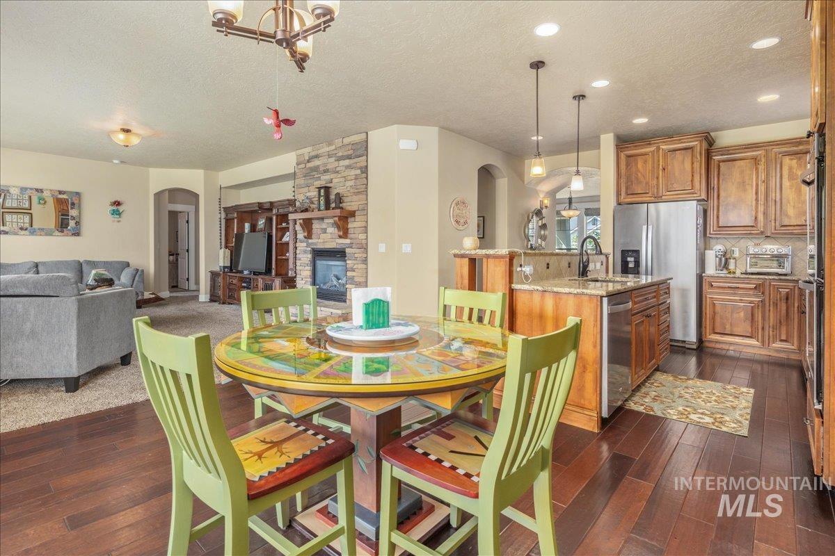 Dining room with arched walkways, a stone fireplace, a textured ceiling, and dark wood finished floors