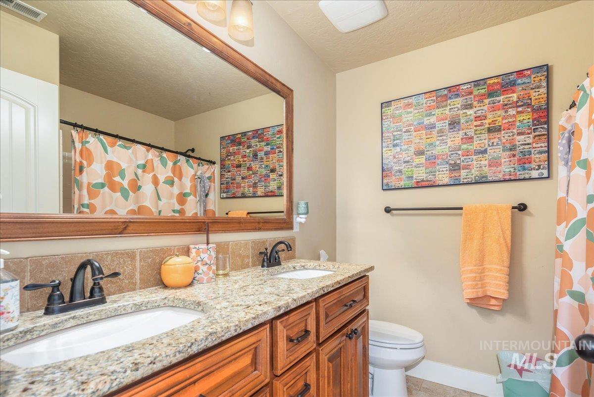 Full bath featuring double vanity, a textured ceiling, backsplash, and a shower with curtain