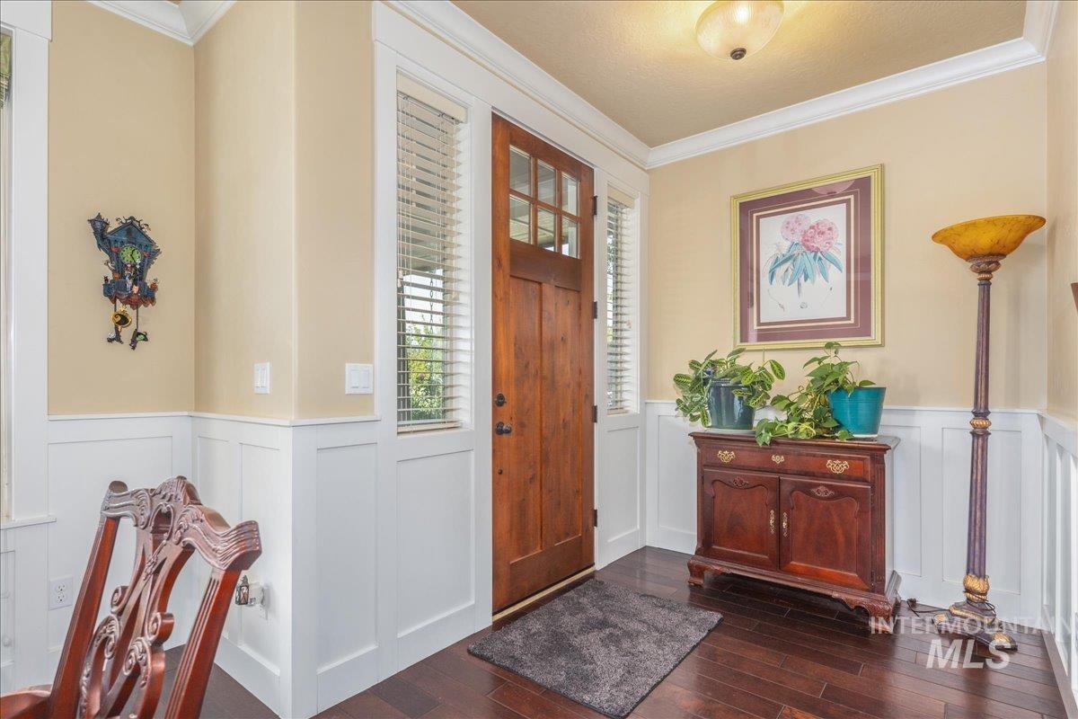 Foyer entrance with crown molding, a decorative wall, dark wood-style flooring, and a wainscoted wall