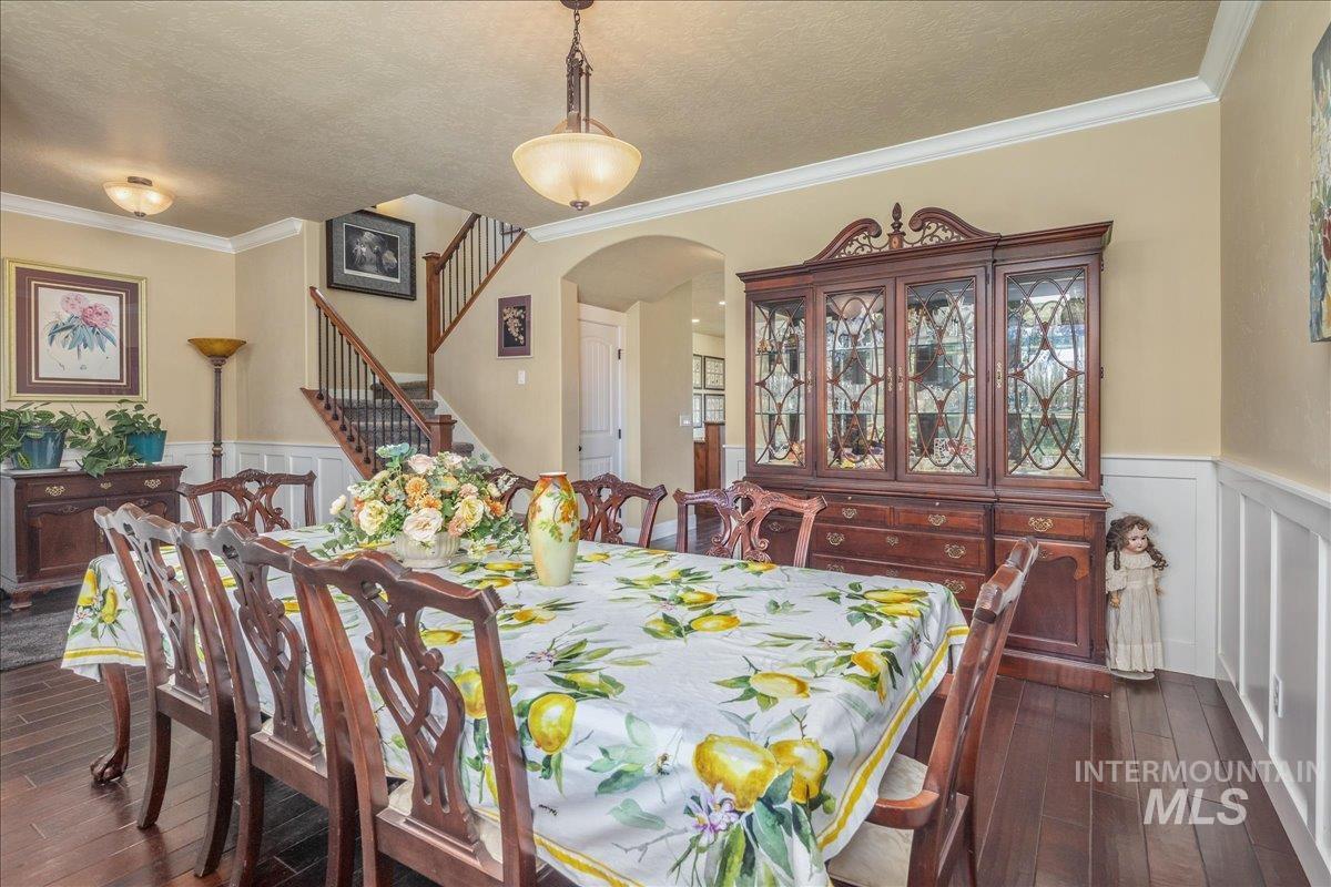 Dining area featuring wainscoting, a decorative wall, crown molding, arched walkways, and dark wood-style flooring