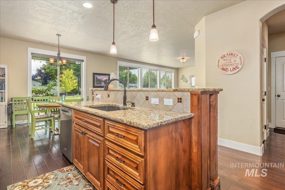 Kitchen featuring dark wood finished floors, light stone counters, brown cabinetry, a textured ceiling, and an island with sink
