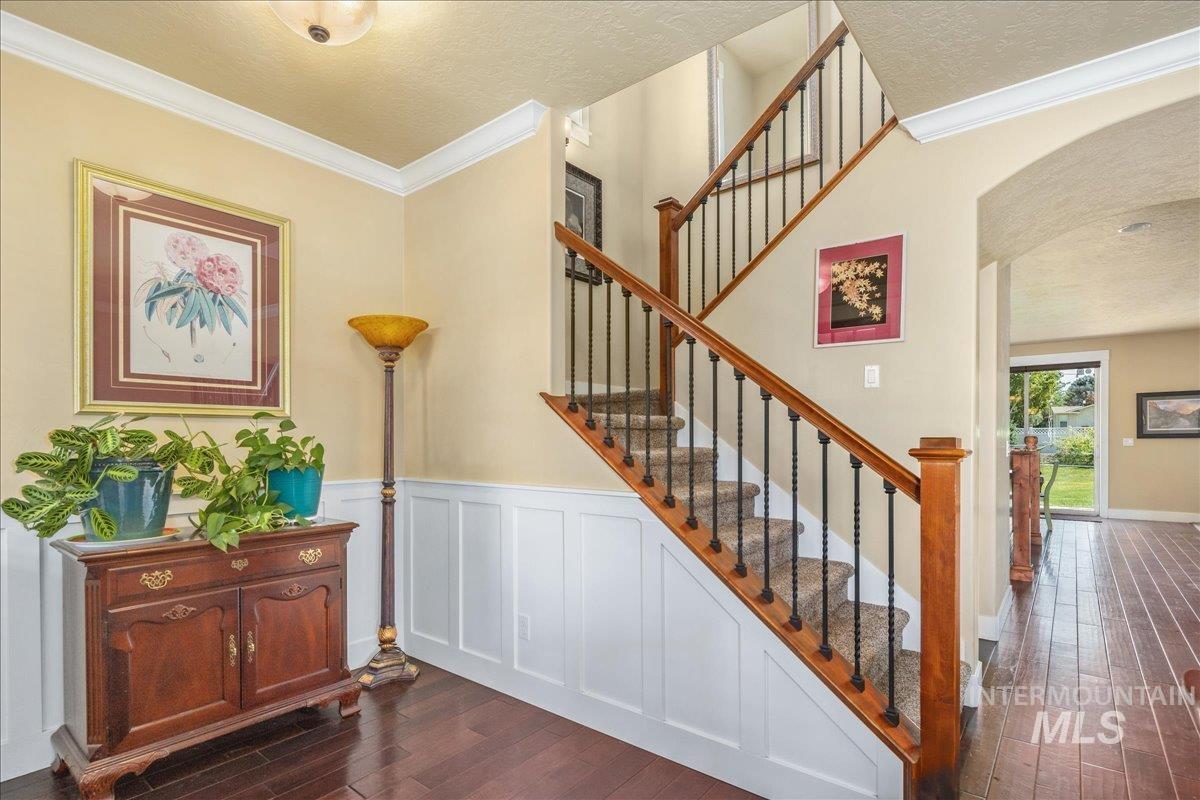 Staircase featuring ornamental molding, wood finished floors, a textured ceiling, arched walkways, and a decorative wall