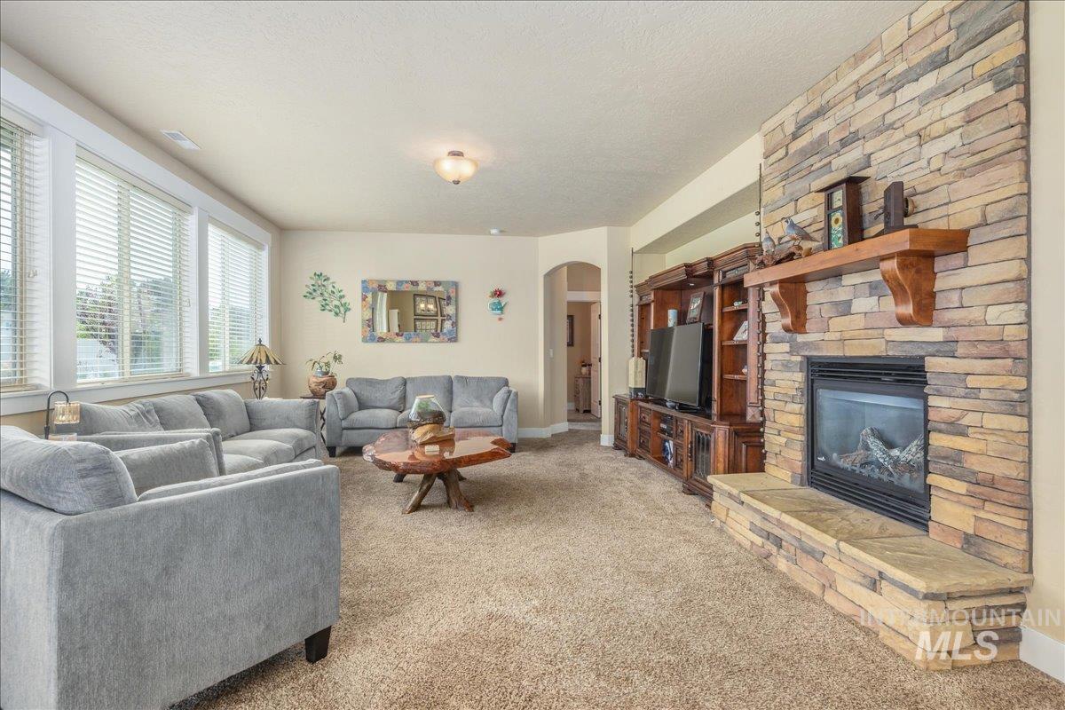 Carpeted living room featuring arched walkways, a fireplace, and a textured ceiling