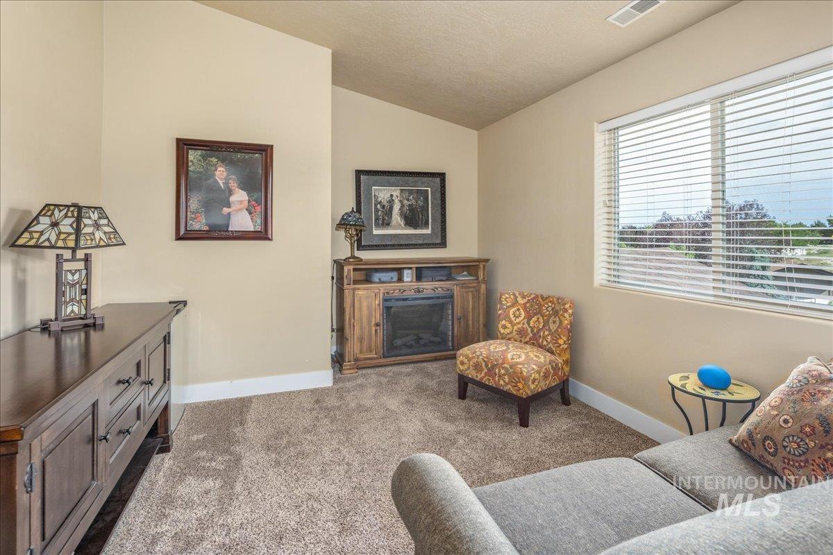Sitting room with vaulted ceiling, dark colored carpet, a textured ceiling, and a fireplace