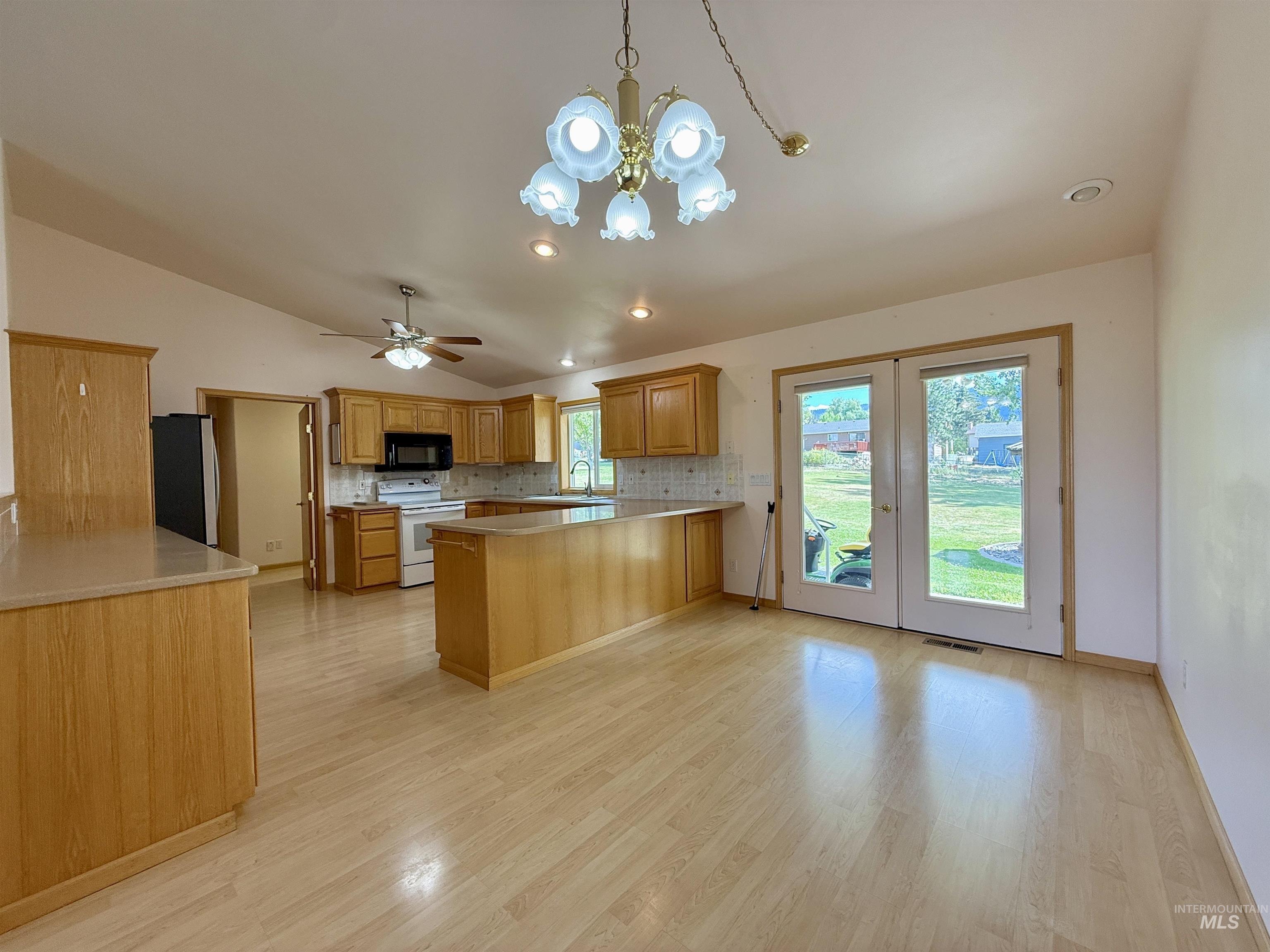 Kitchen with a chandelier, a peninsula, backsplash, freestanding refrigerator, and white electric stove