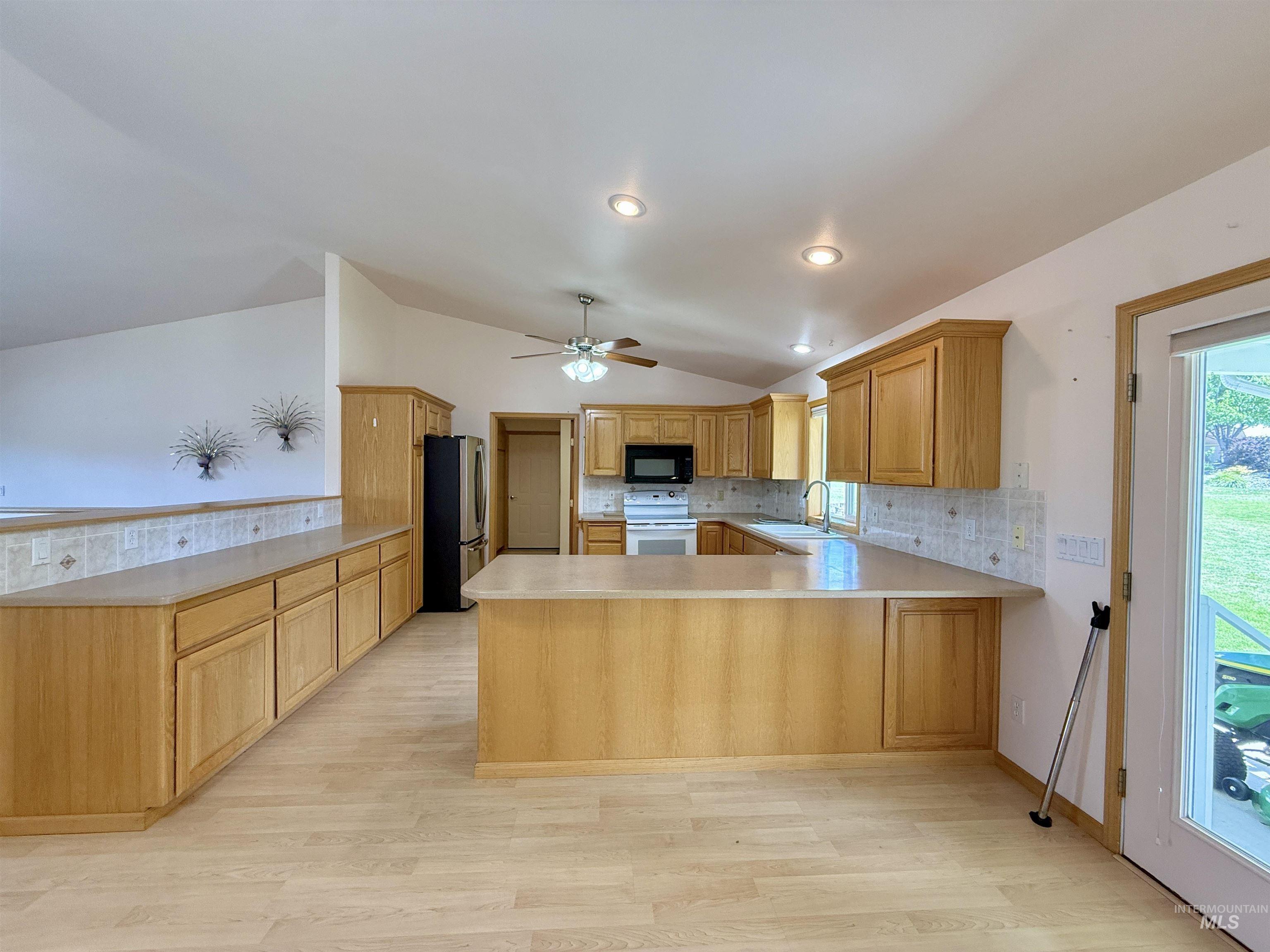 Kitchen featuring a peninsula, lofted ceiling, freestanding refrigerator, plenty of natural light, and light countertops