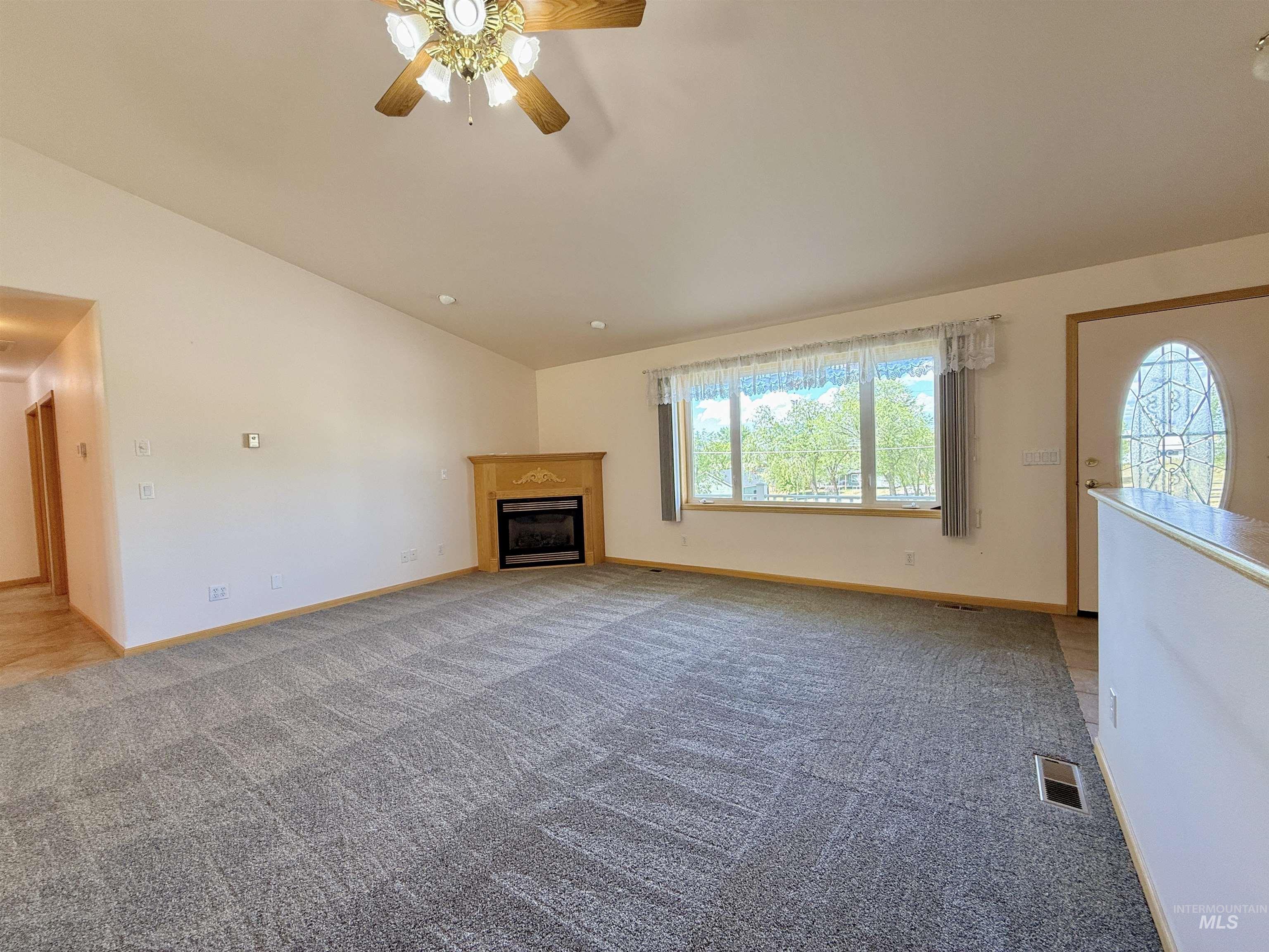 Unfurnished living room with a fireplace, light carpet, ceiling fan, and lofted ceiling