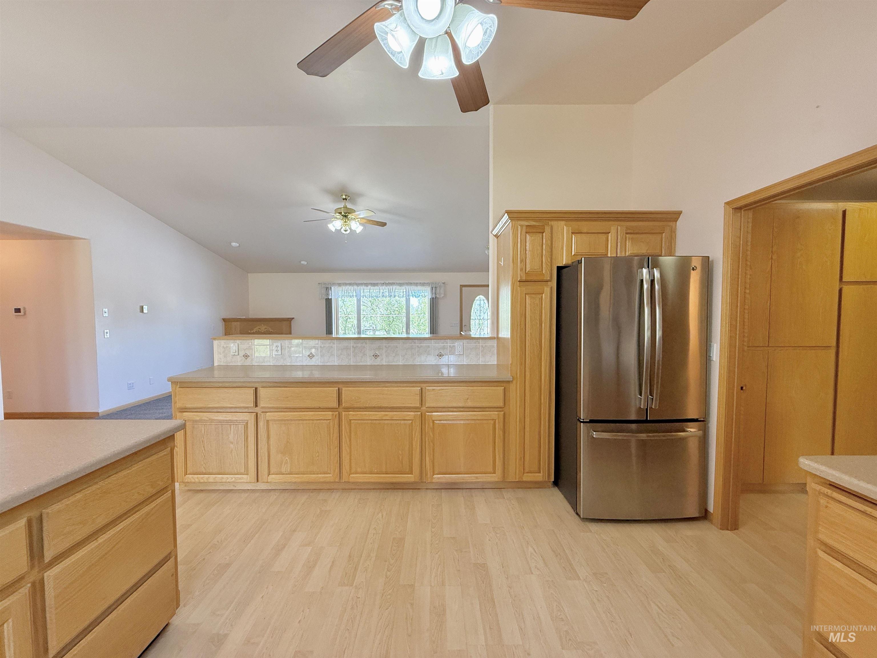 Kitchen with freestanding refrigerator, light countertops, light wood-type flooring, light brown cabinets, and lofted ceiling