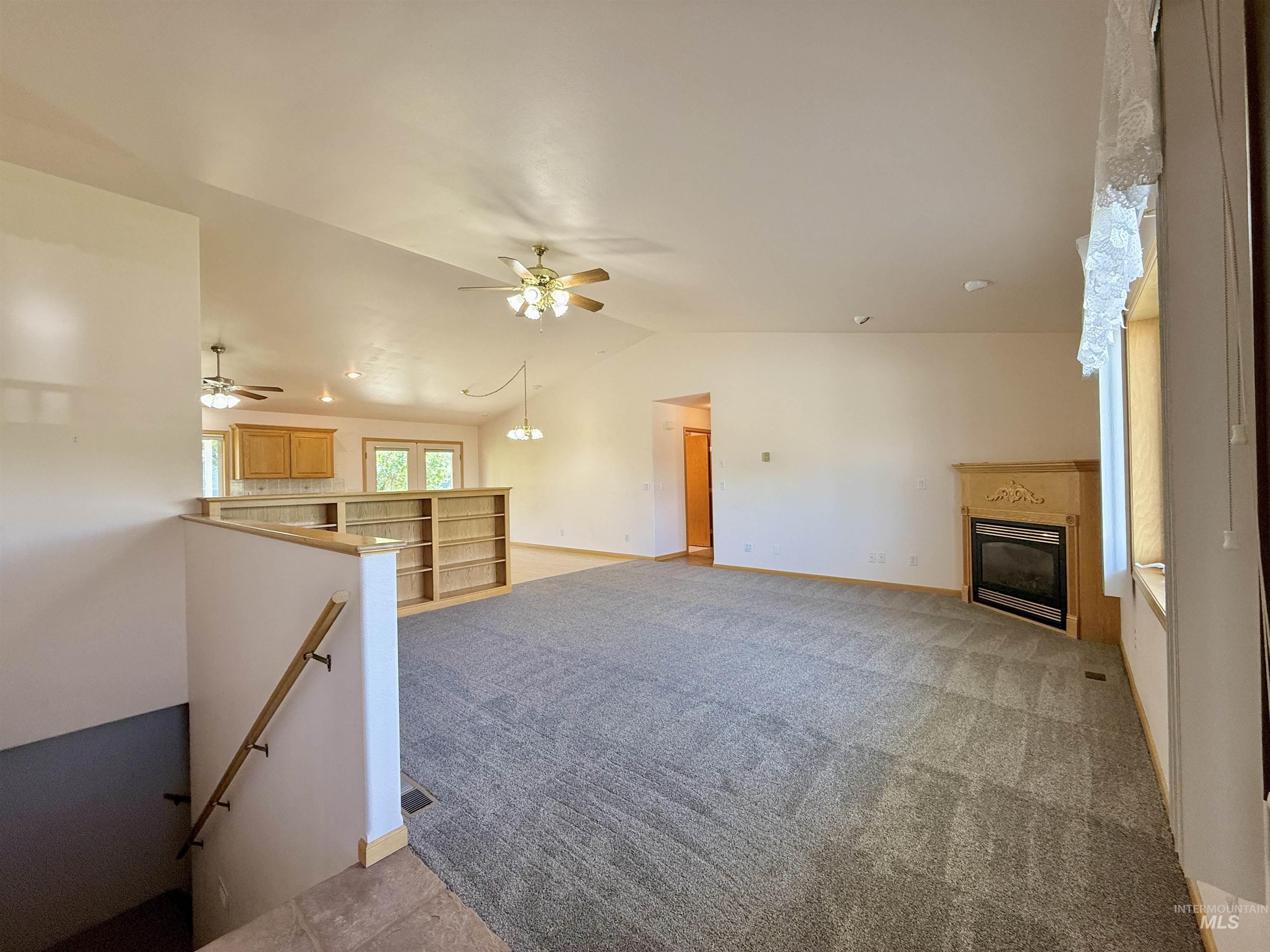 Unfurnished living room with vaulted ceiling, a glass covered fireplace, ceiling fan, and light colored carpet