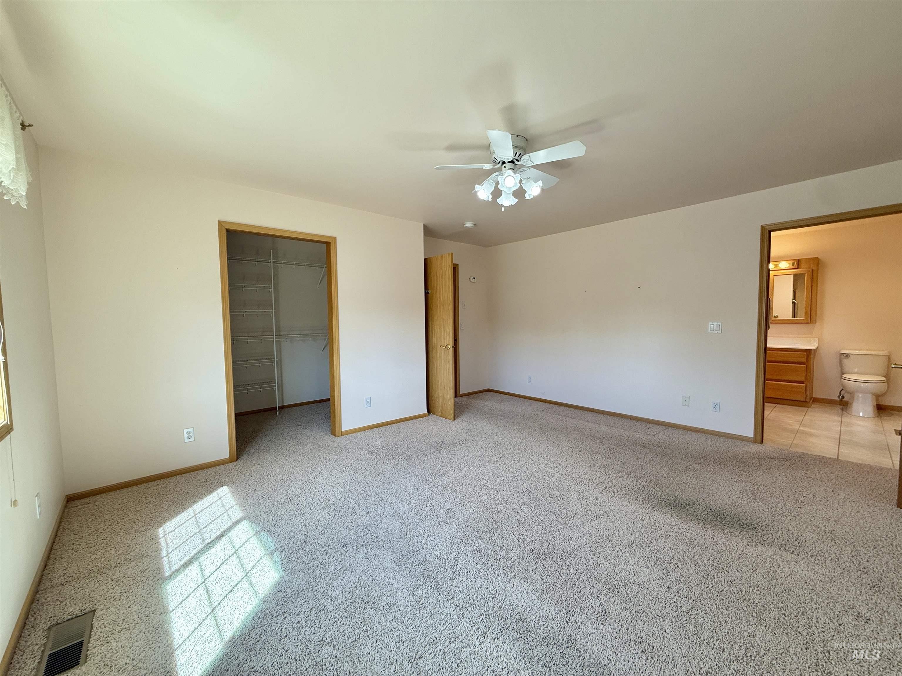 Unfurnished bedroom featuring light colored carpet, a spacious closet, a ceiling fan, and ensuite bathroom