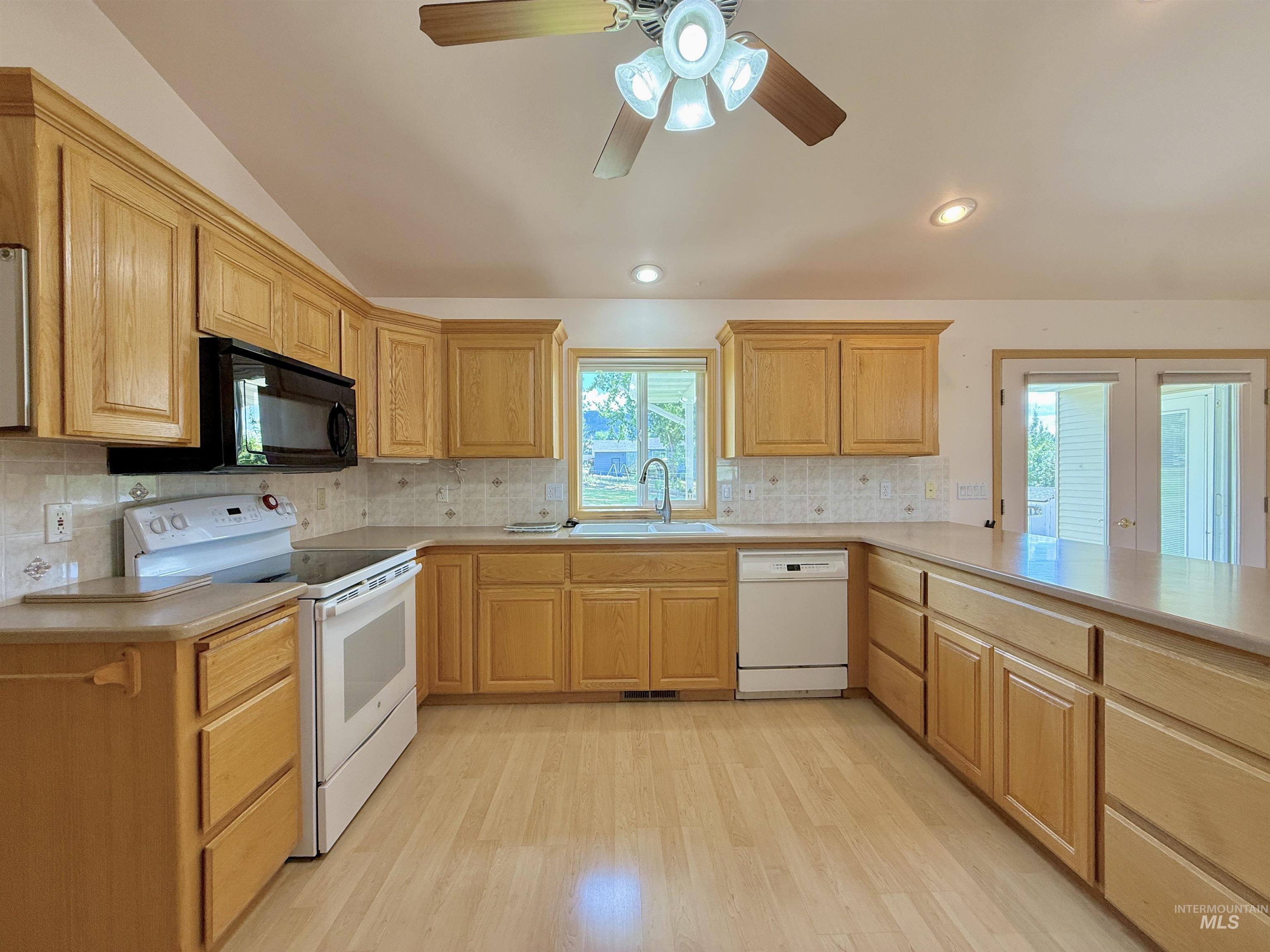 Kitchen with white appliances, lofted ceiling, light wood-type flooring, light countertops, and decorative backsplash