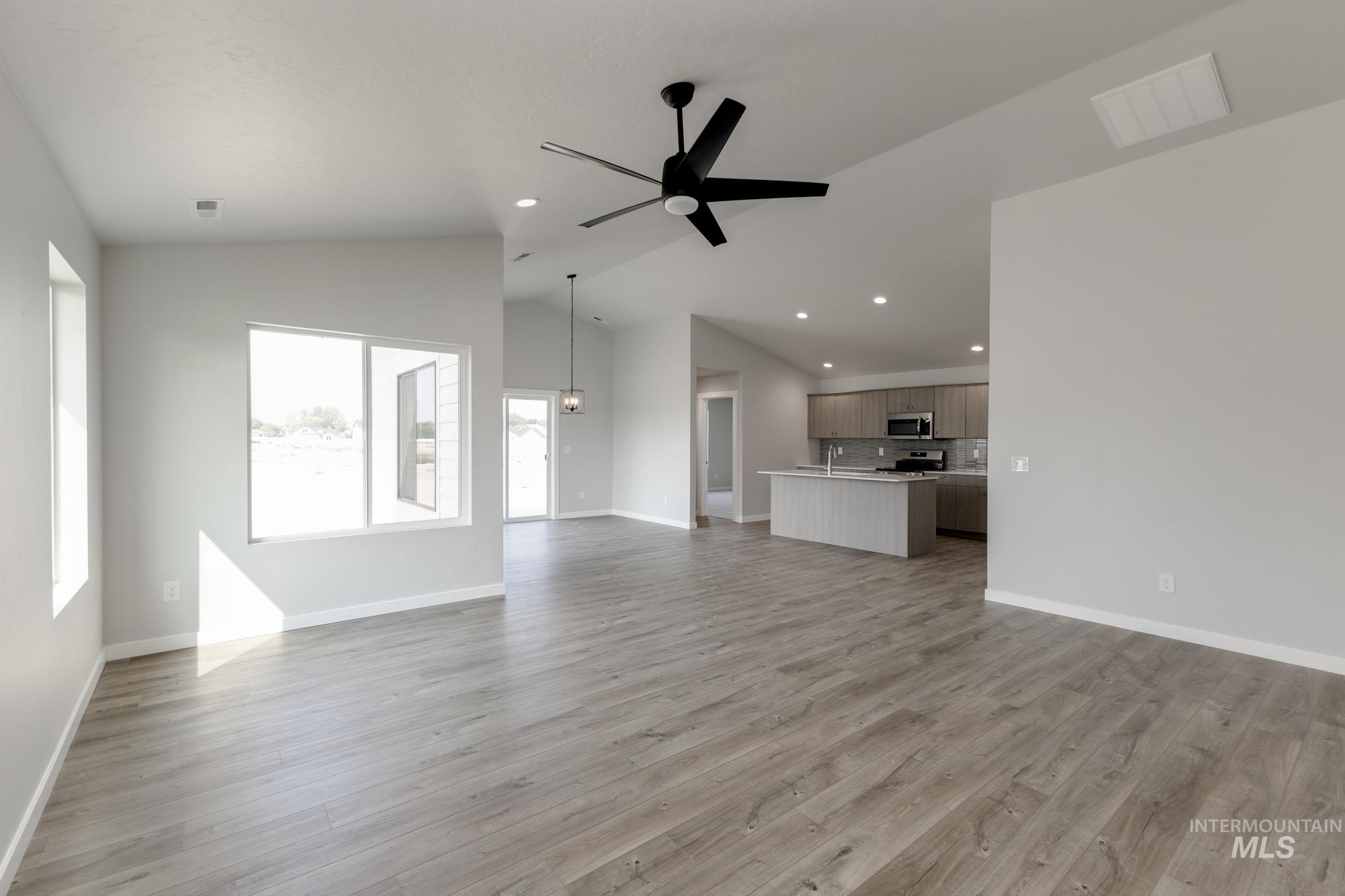 Unfurnished living room featuring ceiling fan, light wood finished floors, lofted ceiling, and recessed lighting