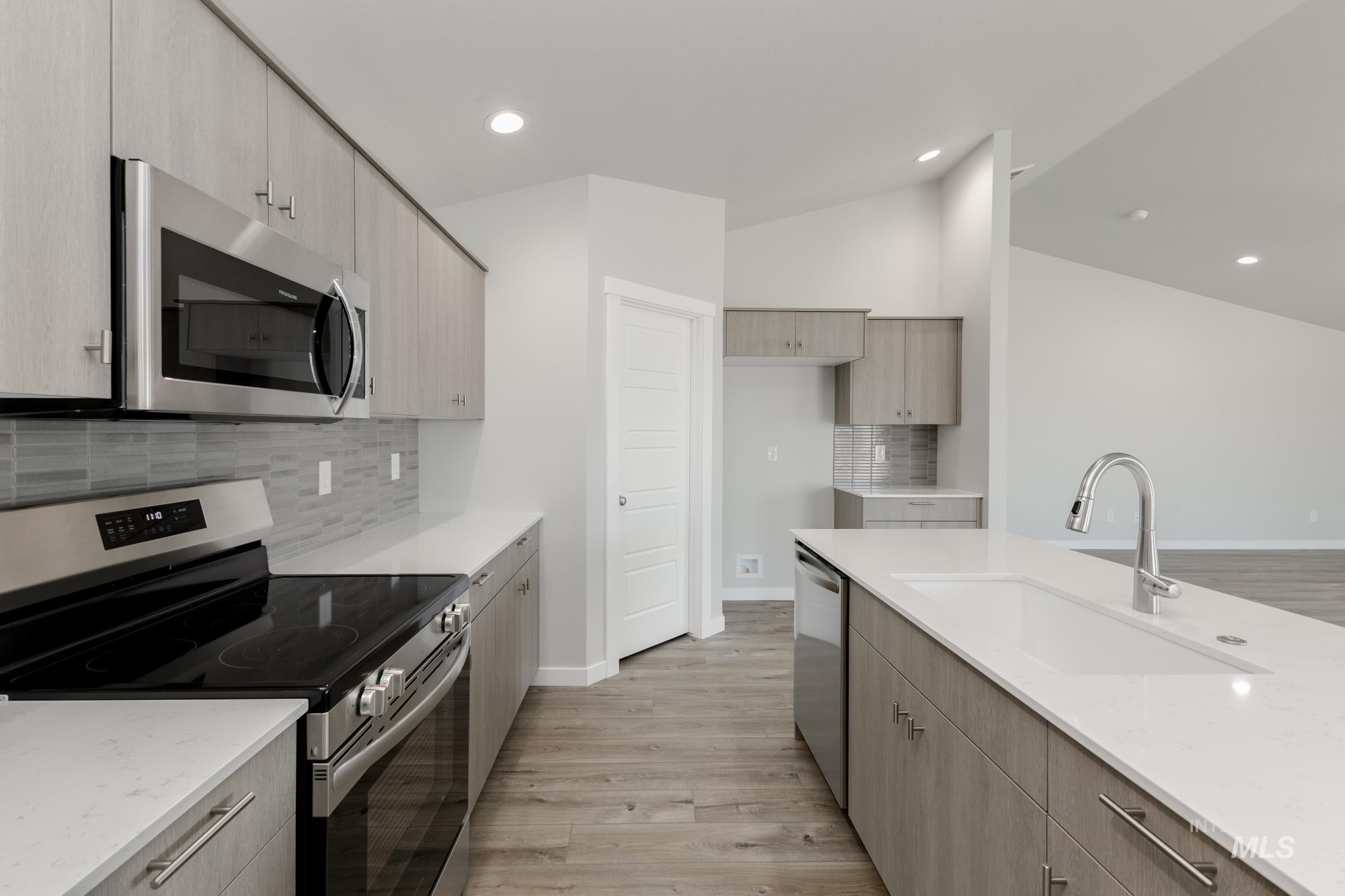 Kitchen featuring appliances with stainless steel finishes, tasteful backsplash, light wood-style floors, light stone counters, and recessed lighting