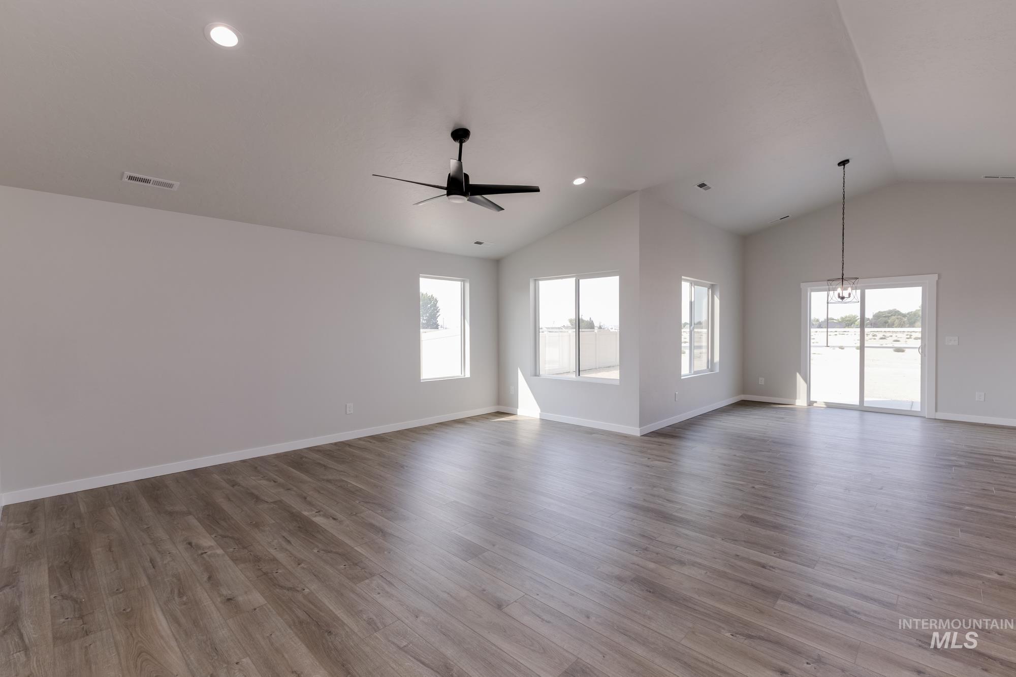 Unfurnished living room featuring healthy amount of natural light, light wood finished floors, ceiling fan, recessed lighting, and high vaulted ceiling