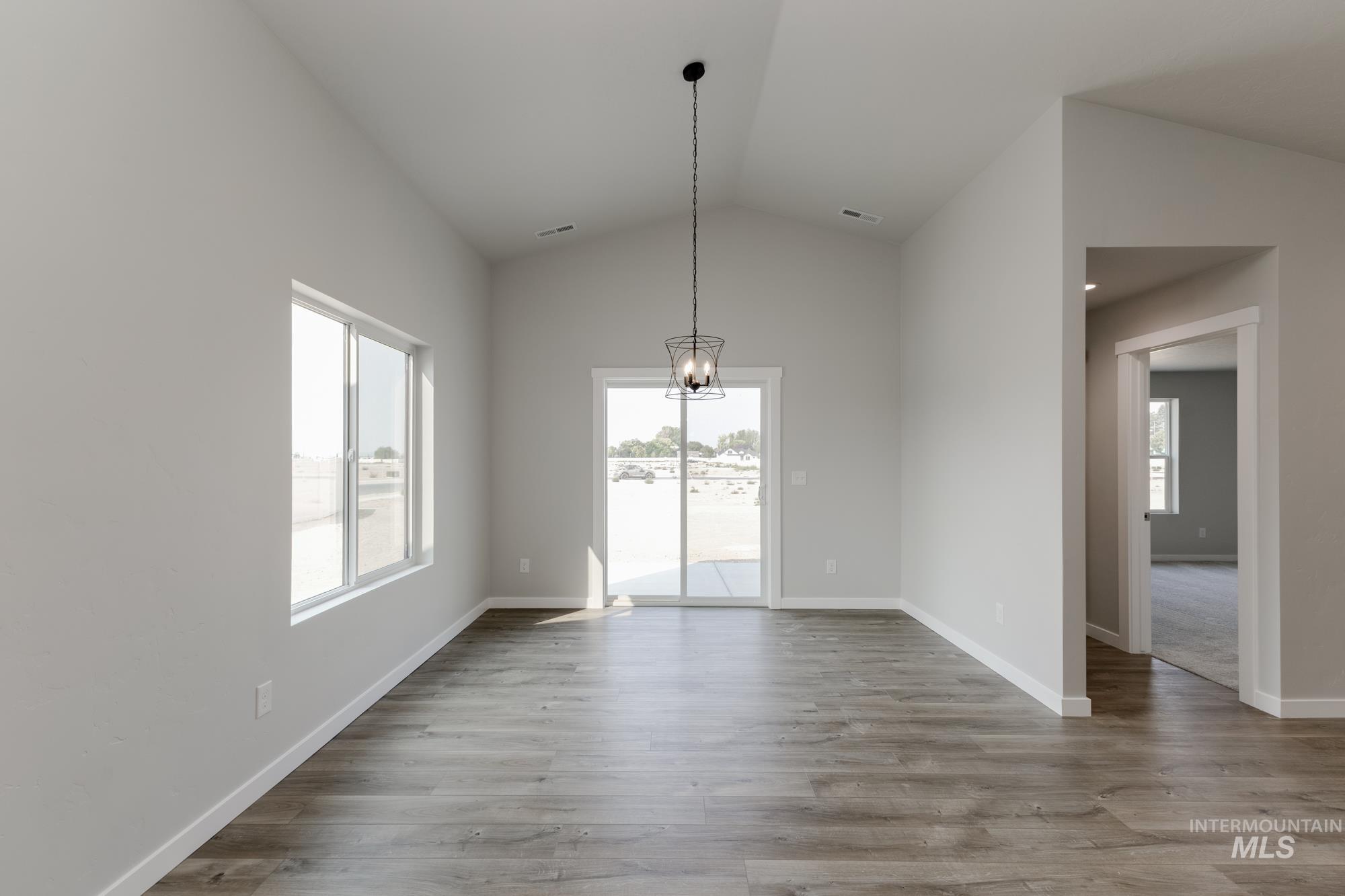 Unfurnished dining area with healthy amount of natural light, lofted ceiling, a chandelier, and wood finished floors