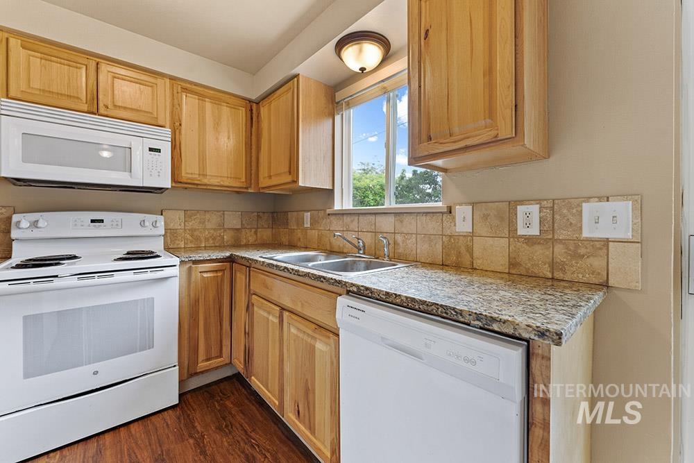 Kitchen with white appliances, dark wood-style flooring, and light countertops