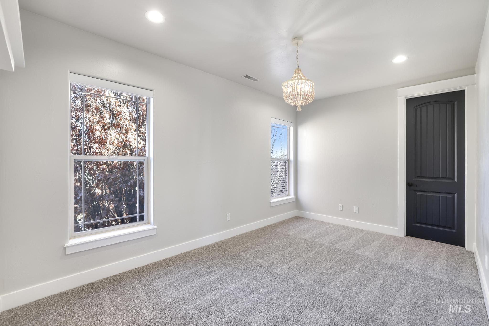 Carpeted empty room featuring baseboards and a chandelier