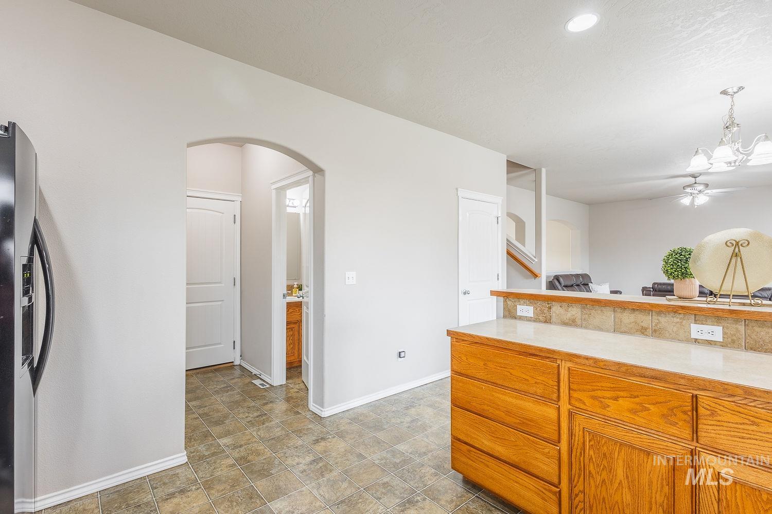 Kitchen featuring light countertops, stainless steel fridge with ice dispenser, brown cabinetry, pendant lighting, and arched walkways