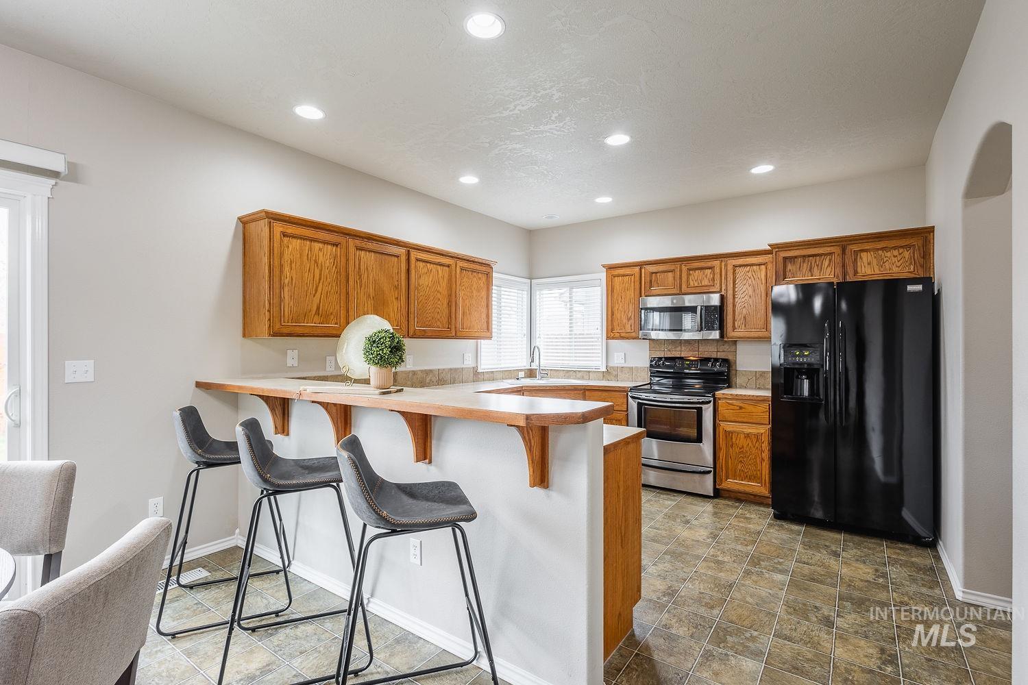 Kitchen featuring brown cabinetry, stainless steel appliances, a peninsula, a breakfast bar area, and light countertops