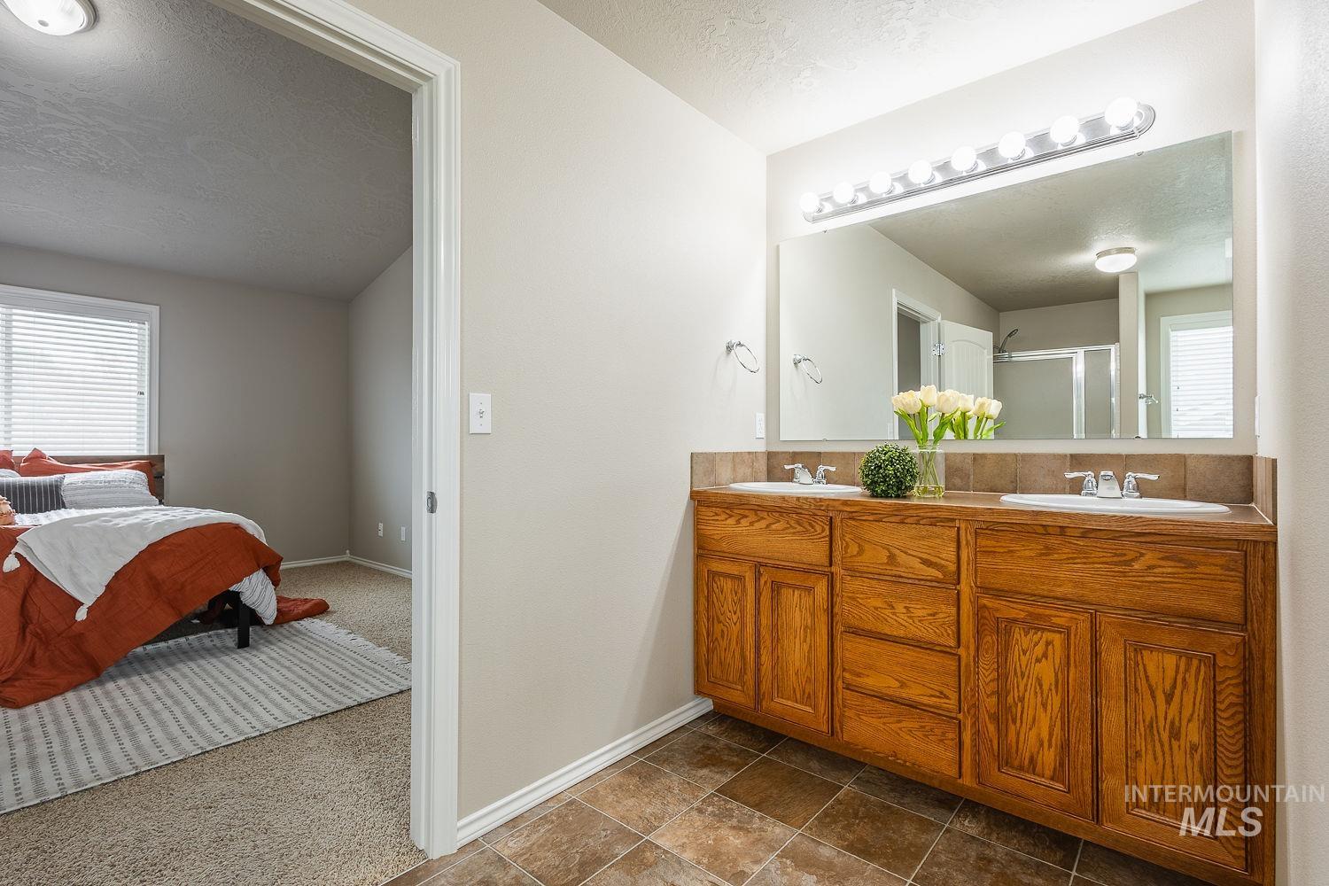 Ensuite bathroom with a textured ceiling, dark colored carpet, double vanity, and a shower stall