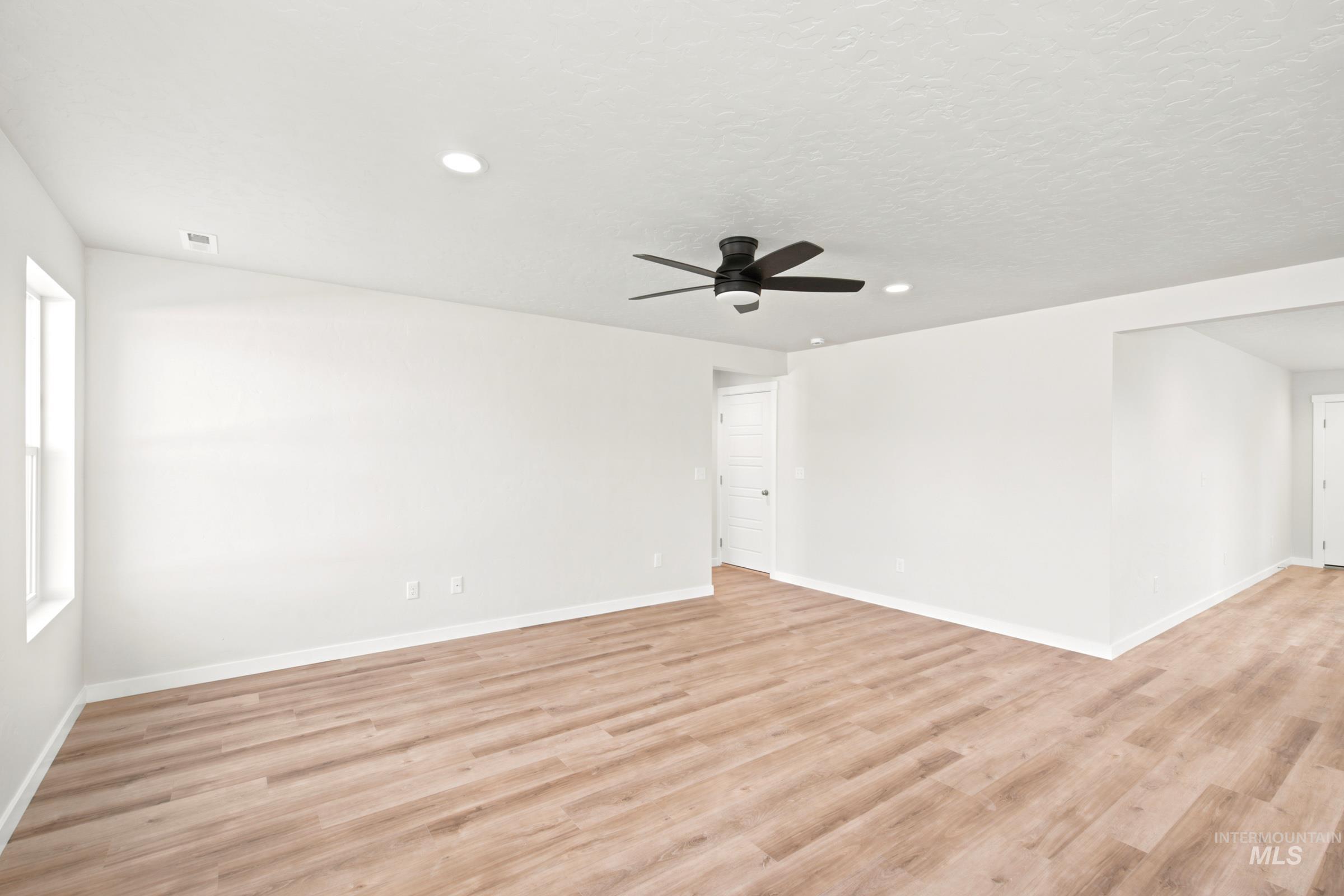 Spacious room featuring wood-finish flooring, white walls, and a ceiling fan with integrated lighting