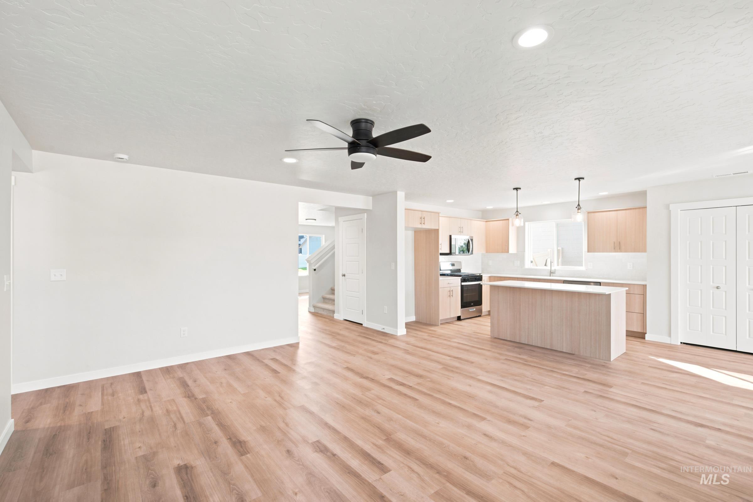 Open-concept living space featuring wood-finish flooring, a contemporary ceiling fan, recessed lighting, and a modern kitchen with a light wood-finish island and cabinetry