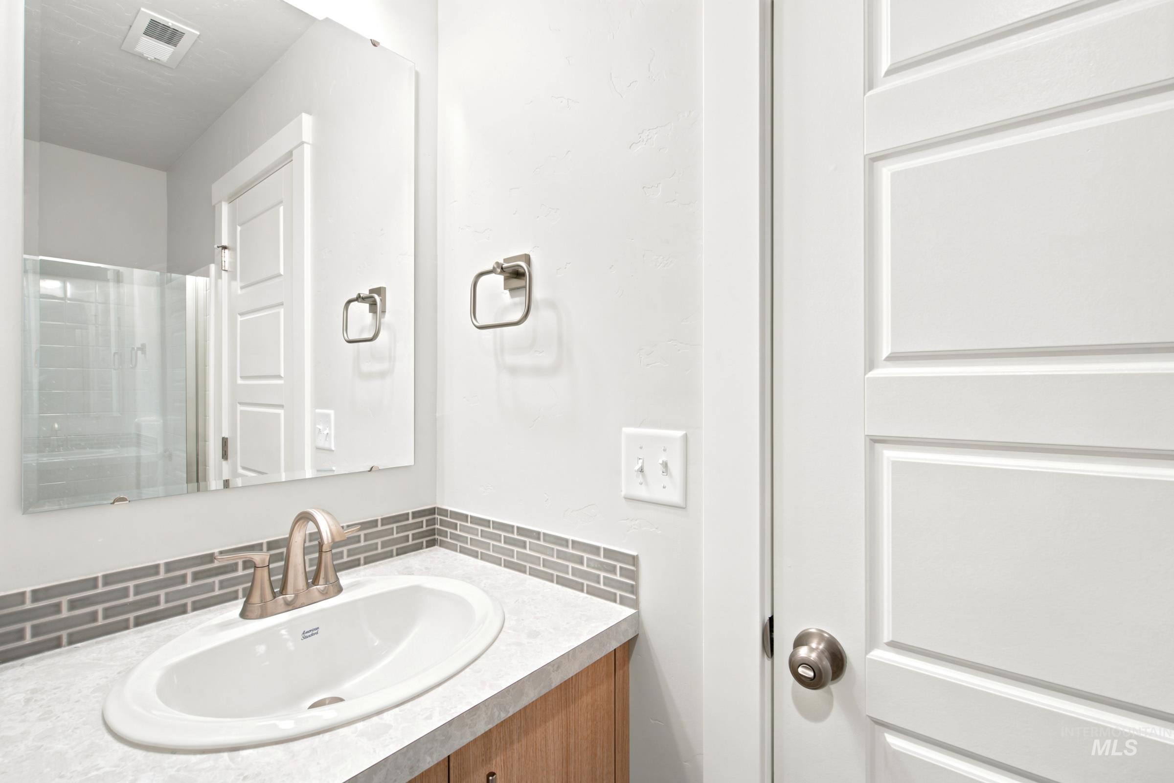 Bathroom vanity featuring an oval undermount sink, brushed nickel faucet, and a grey mosaic tile backsplash