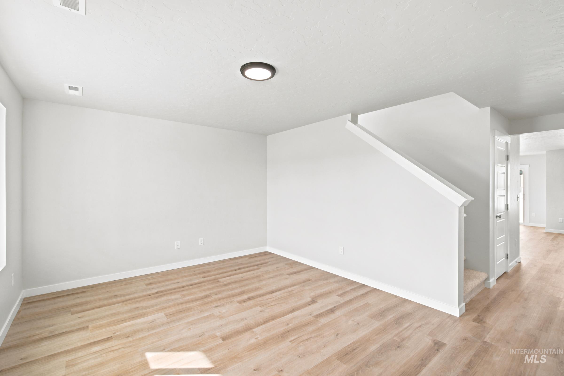 Spacious interior featuring light wood-finish flooring, white baseboards, and a contemporary flush-mount ceiling light
