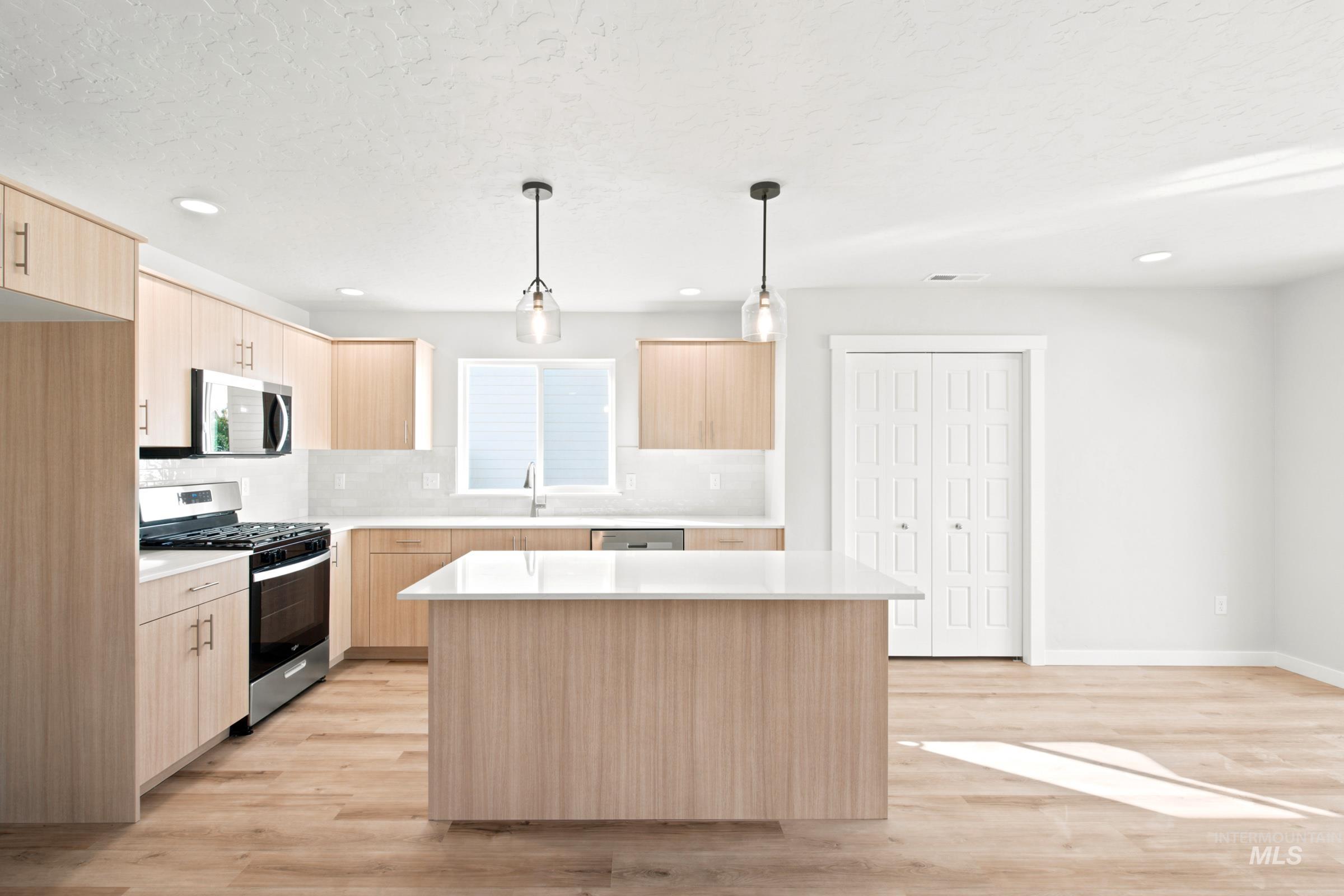 Kitchen featuring light wood-finish cabinetry, stainless steel appliances, a white subway tile backsplash, and a central island with a white countertop