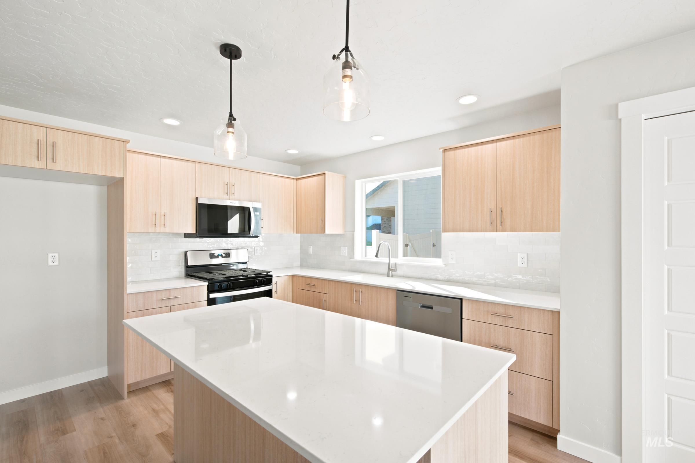 Kitchen featuring a large central island with a white countertop, light wood-finish cabinetry, stainless steel appliances, and a white tile backsplash
