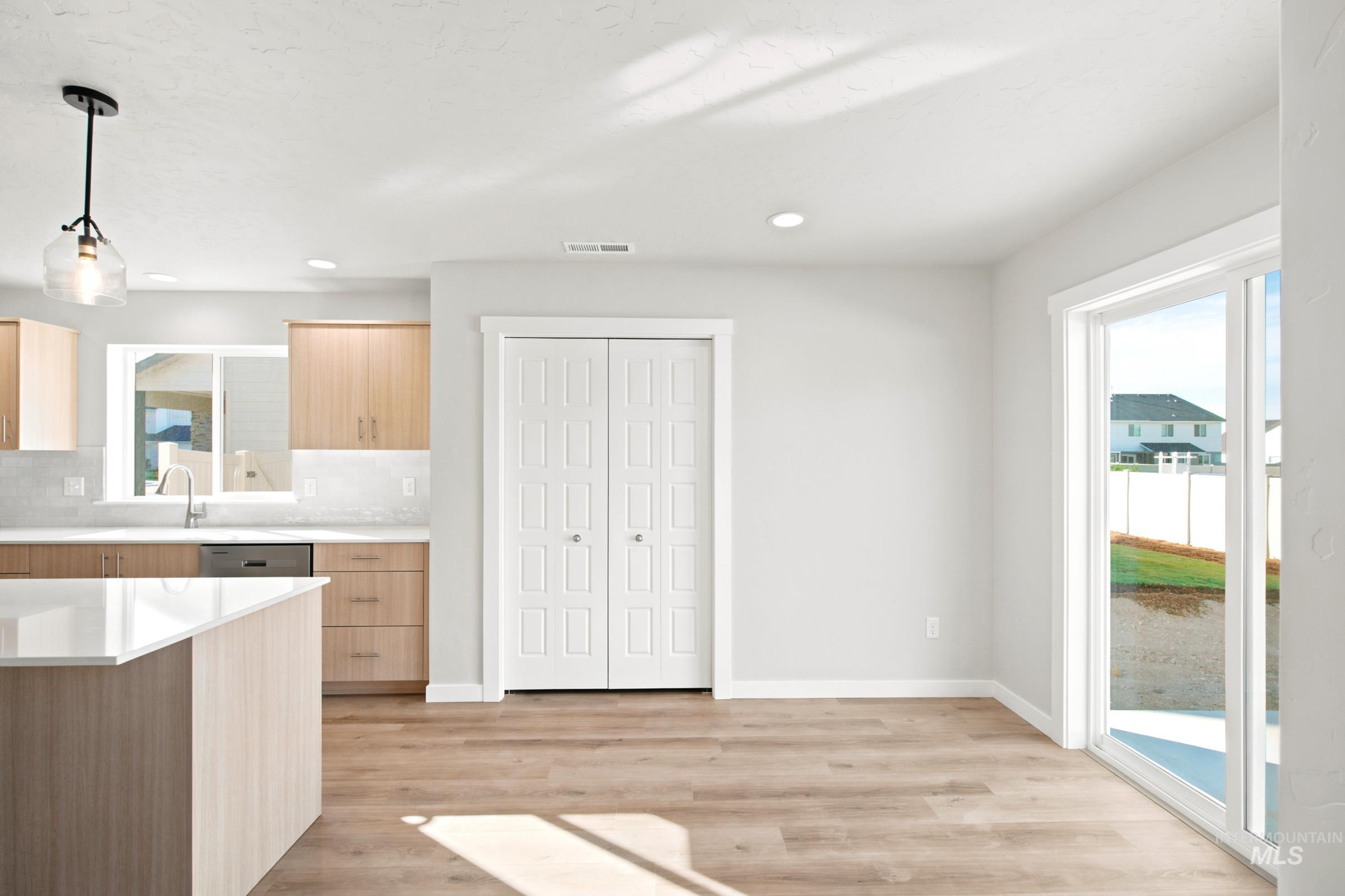 Open-concept kitchen and dining area featuring a kitchen island with a light-toned countertop, wood-finish flooring, light wood cabinetry, and a large window above the sink
