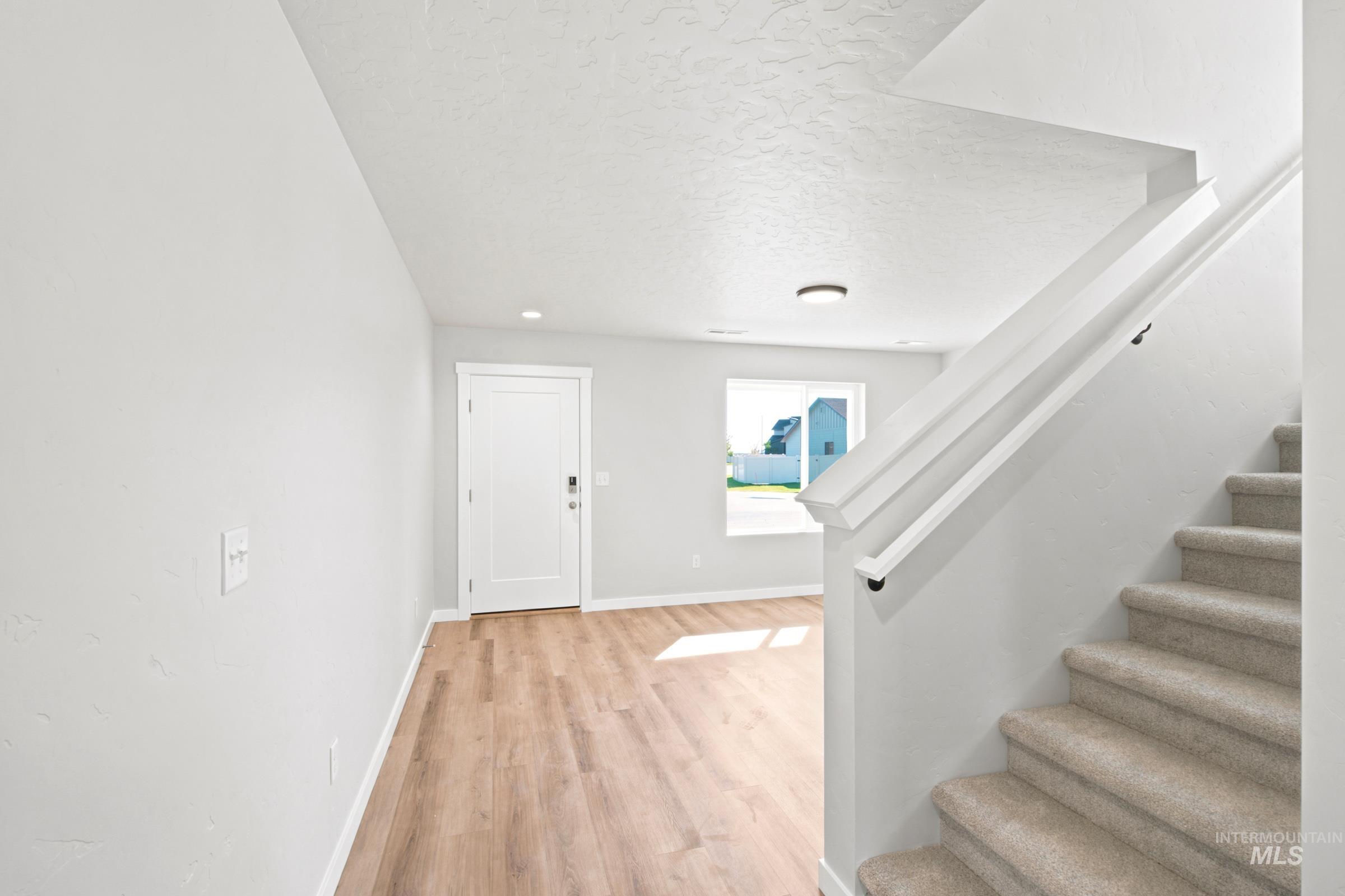 Foyer featuring wood-finish flooring, a white paneled door, recessed ceiling lighting, and a carpeted staircase with white railings