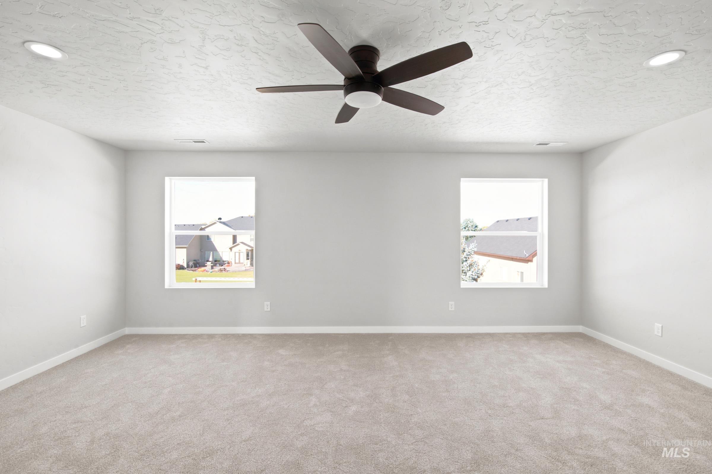 Spacious room featuring neutral carpet, two windows, two recessed lights, and a ceiling fan with integrated lighting