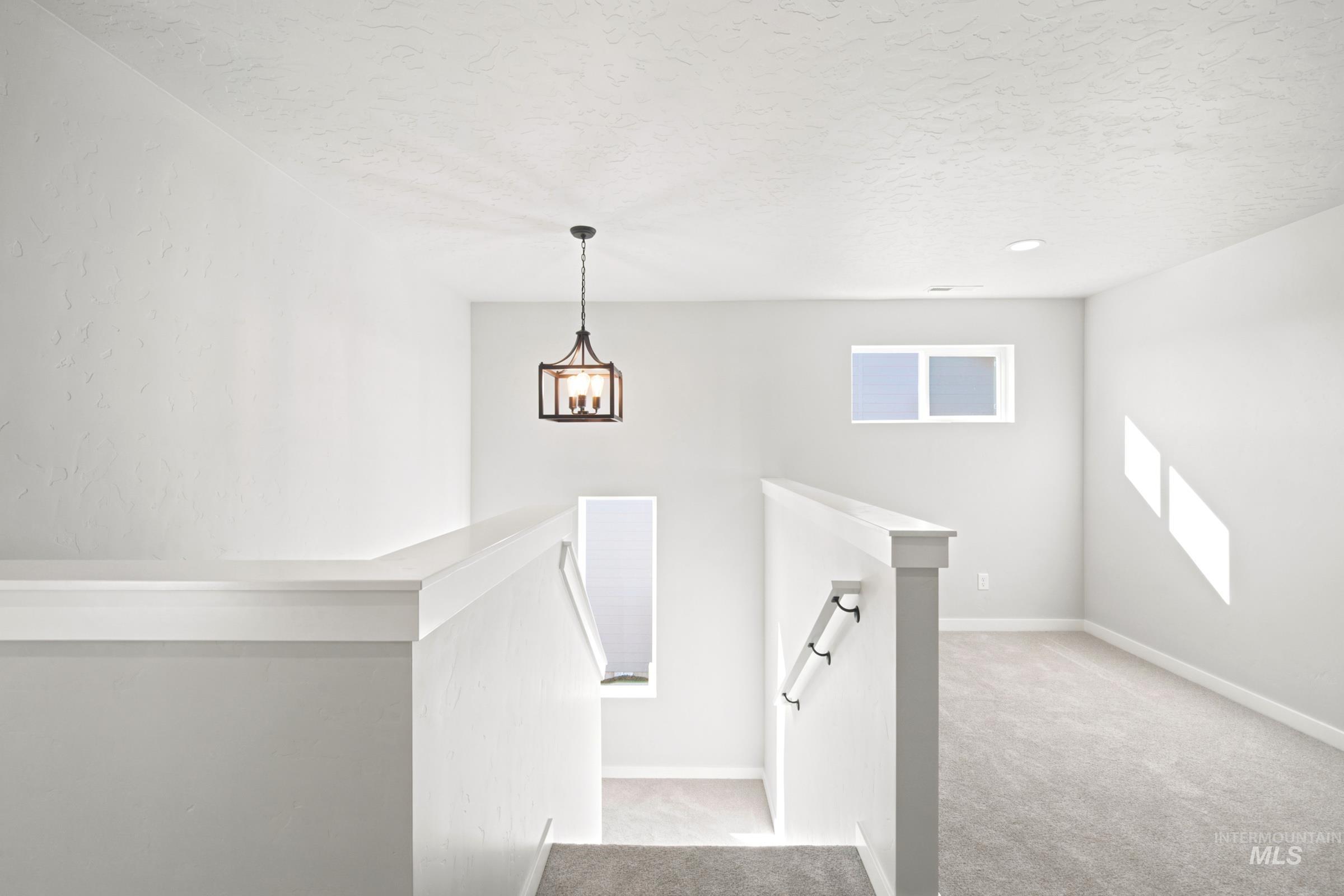 Open landing area featuring a contemporary chandelier, white painted walls, light gray carpeting, and a rectangular window