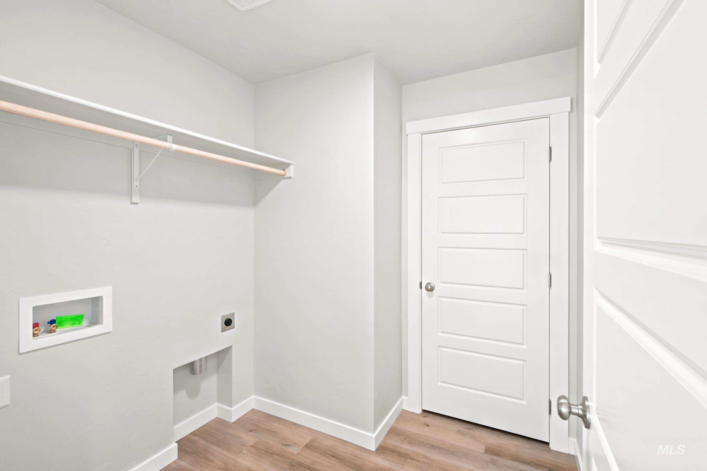 Laundry area featuring wood-finish flooring, a white shelving unit with a hanging rod, appliance hookups, and a contemporary five-panel interior door