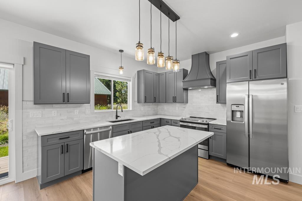 Kitchen with gray cabinets, stainless steel appliances, decorative light fixtures, custom exhaust hood, and recessed lighting