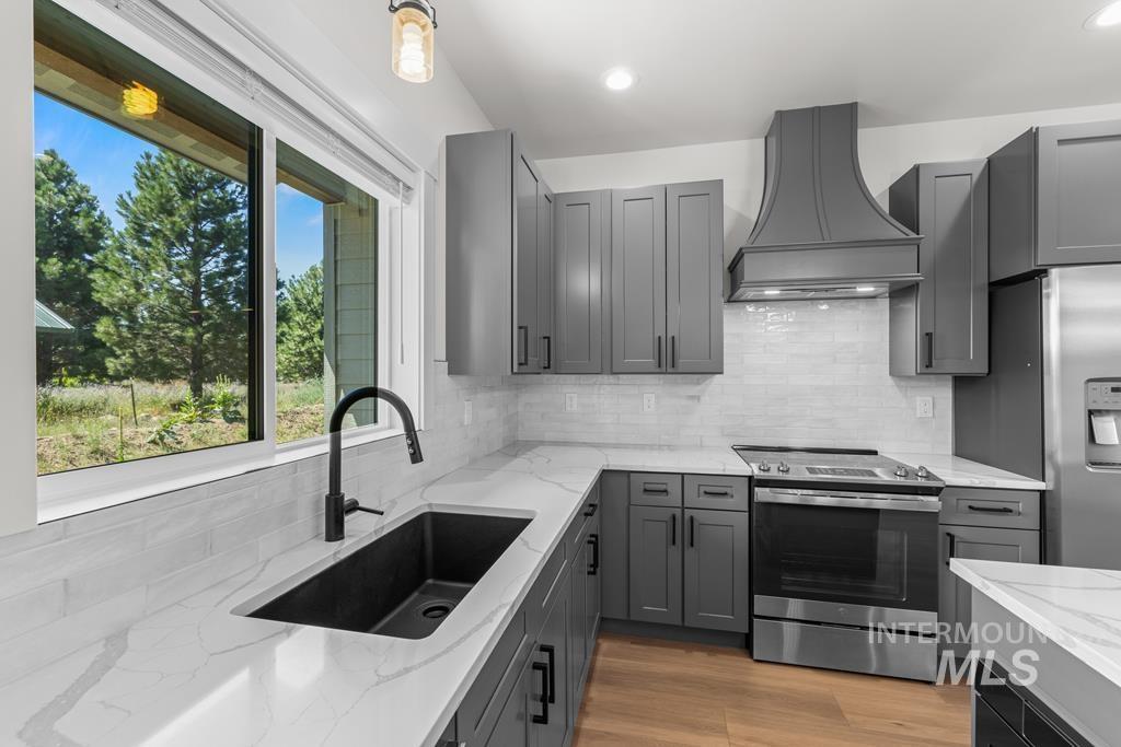 Kitchen featuring tasteful backsplash, stainless steel appliances, light stone countertops, gray cabinets, and custom exhaust hood