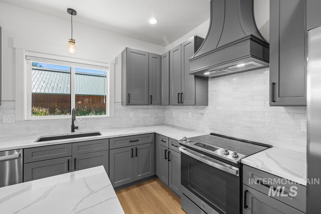 Kitchen with gray cabinetry, appliances with stainless steel finishes, custom exhaust hood, hanging light fixtures, and recessed lighting