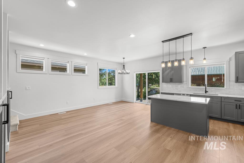 Kitchen featuring gray cabinets, tasteful backsplash, pendant lighting, light wood-type flooring, and a center island