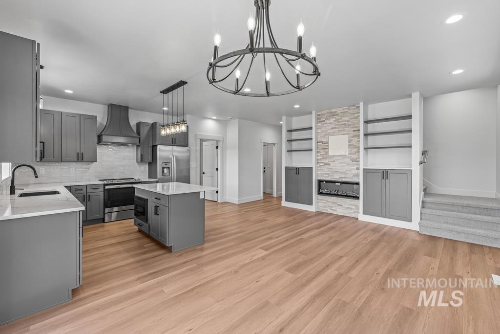 Kitchen with gray cabinetry, premium range hood, stainless steel appliances, light stone countertops, and a center island
