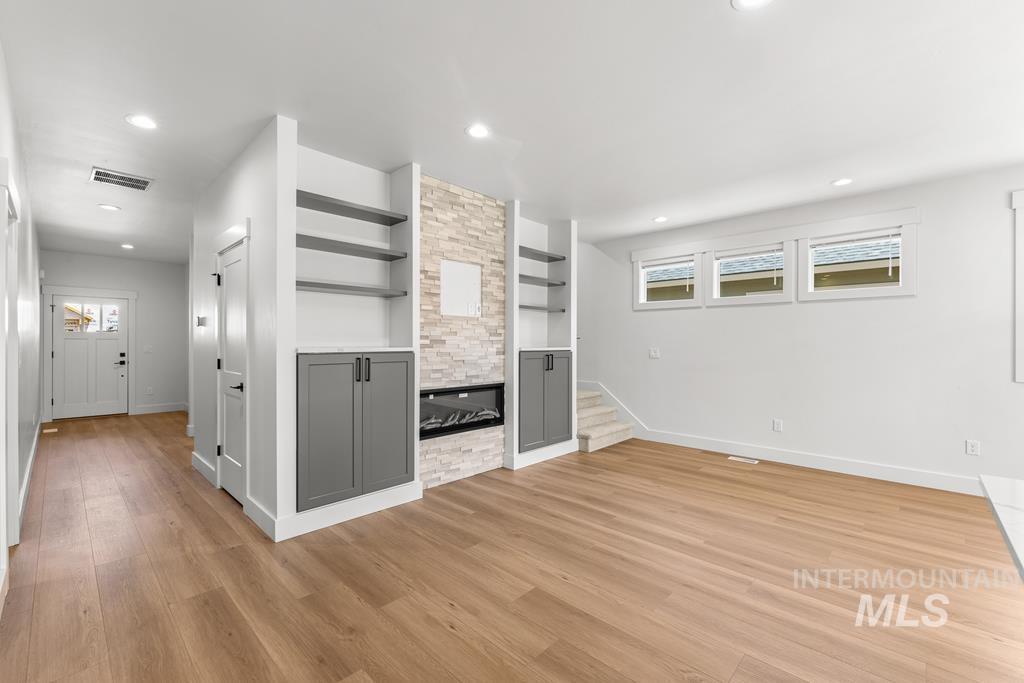 Unfurnished living room featuring recessed lighting, light wood-style flooring, a stone fireplace, and built in shelves