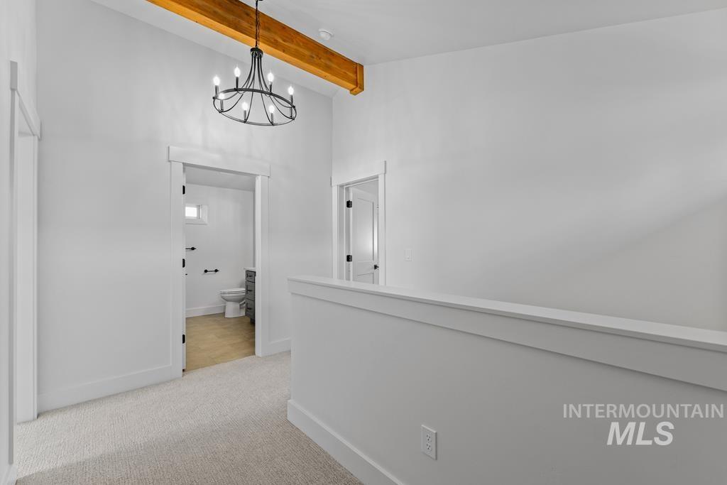 Corridor featuring beam ceiling, light carpet, a chandelier, and high vaulted ceiling
