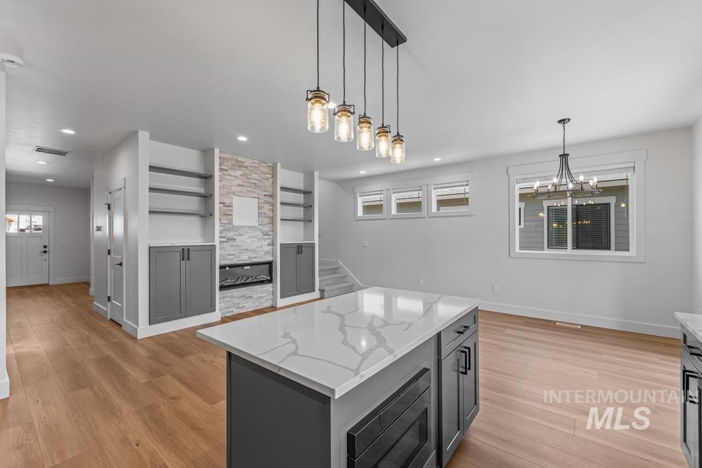 Kitchen featuring gray cabinetry, pendant lighting, light stone countertops, a center island, and light wood-style floors