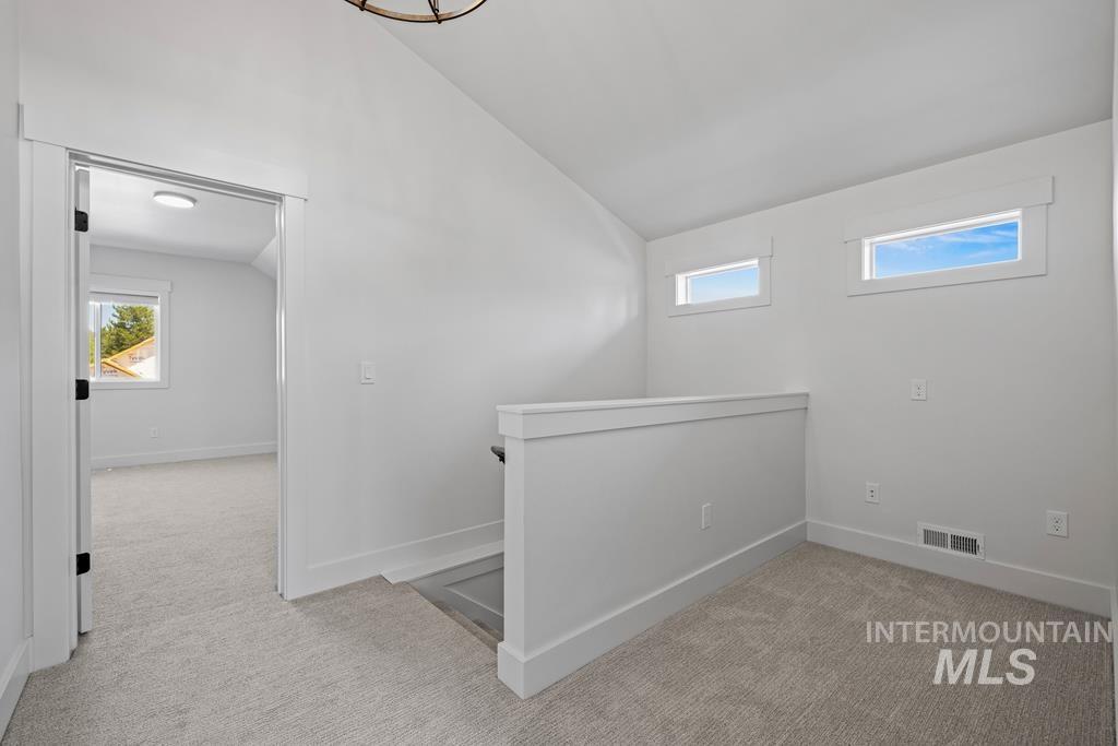 Additional living space with vaulted ceiling and light colored carpet