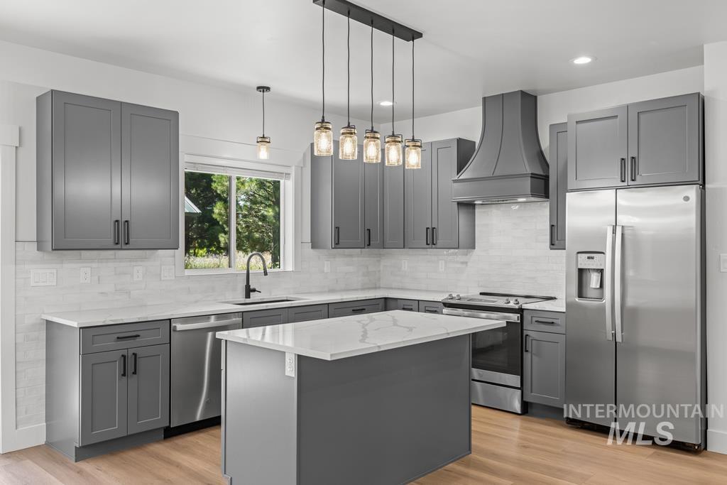 Kitchen with gray cabinetry, stainless steel appliances, premium range hood, decorative light fixtures, and light wood-style flooring