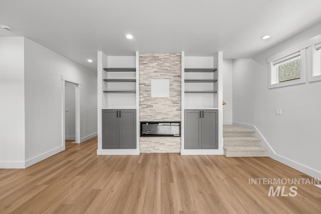 Unfurnished living room featuring recessed lighting, light wood-style floors, stairs, and built in shelves