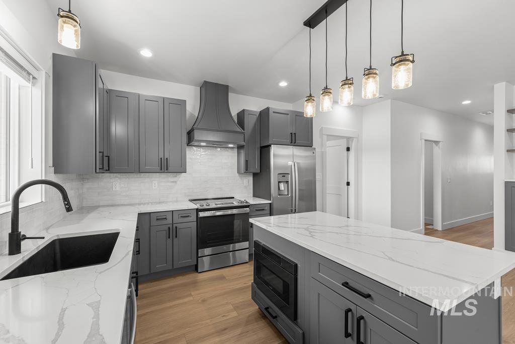 Kitchen with gray cabinets, stainless steel appliances, light stone countertops, pendant lighting, and premium range hood