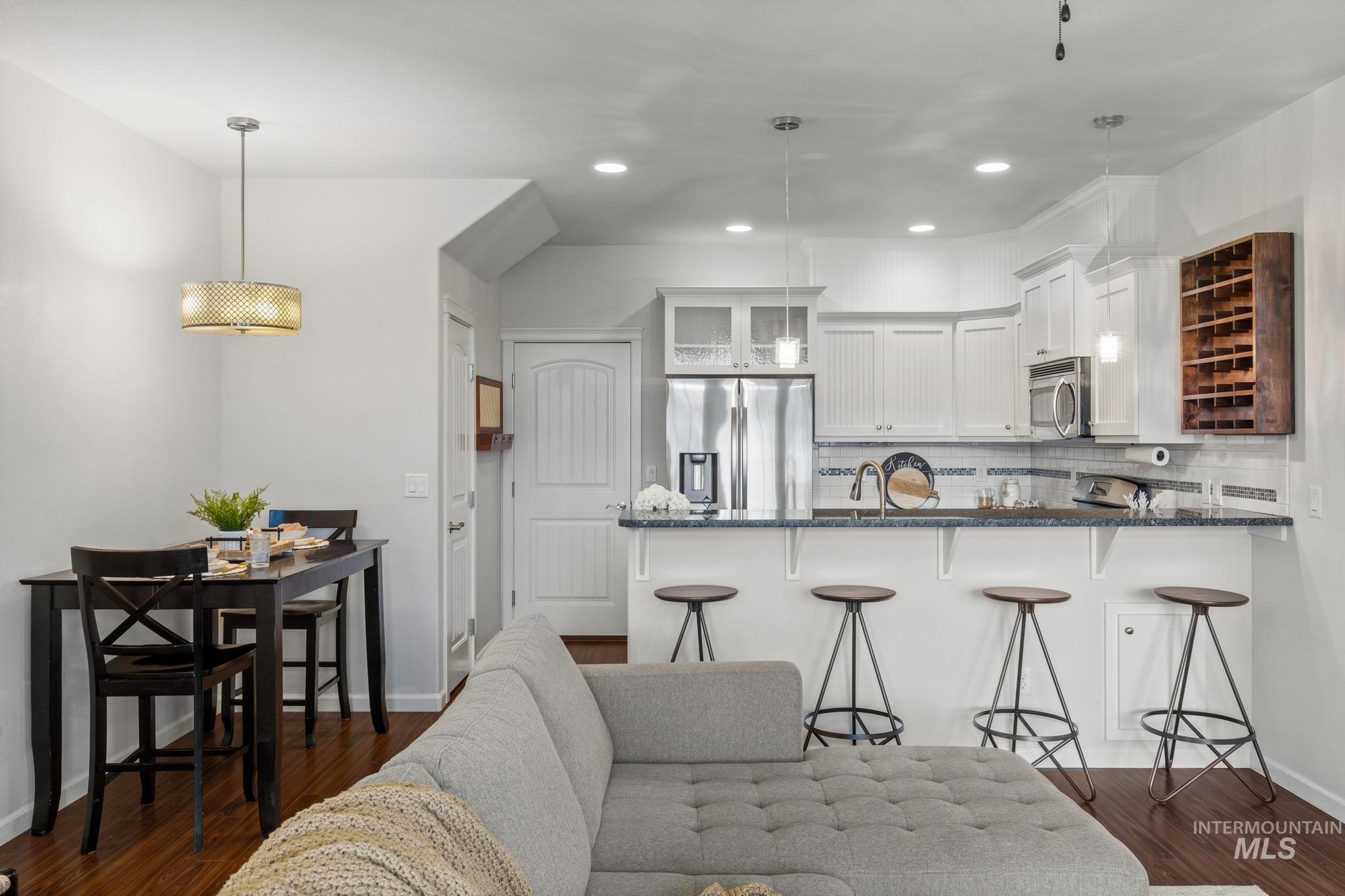 Kitchen with dark stone countertops, a kitchen bar, glass fronted cabinets, stainless steel appliances, and dark wood finished floors