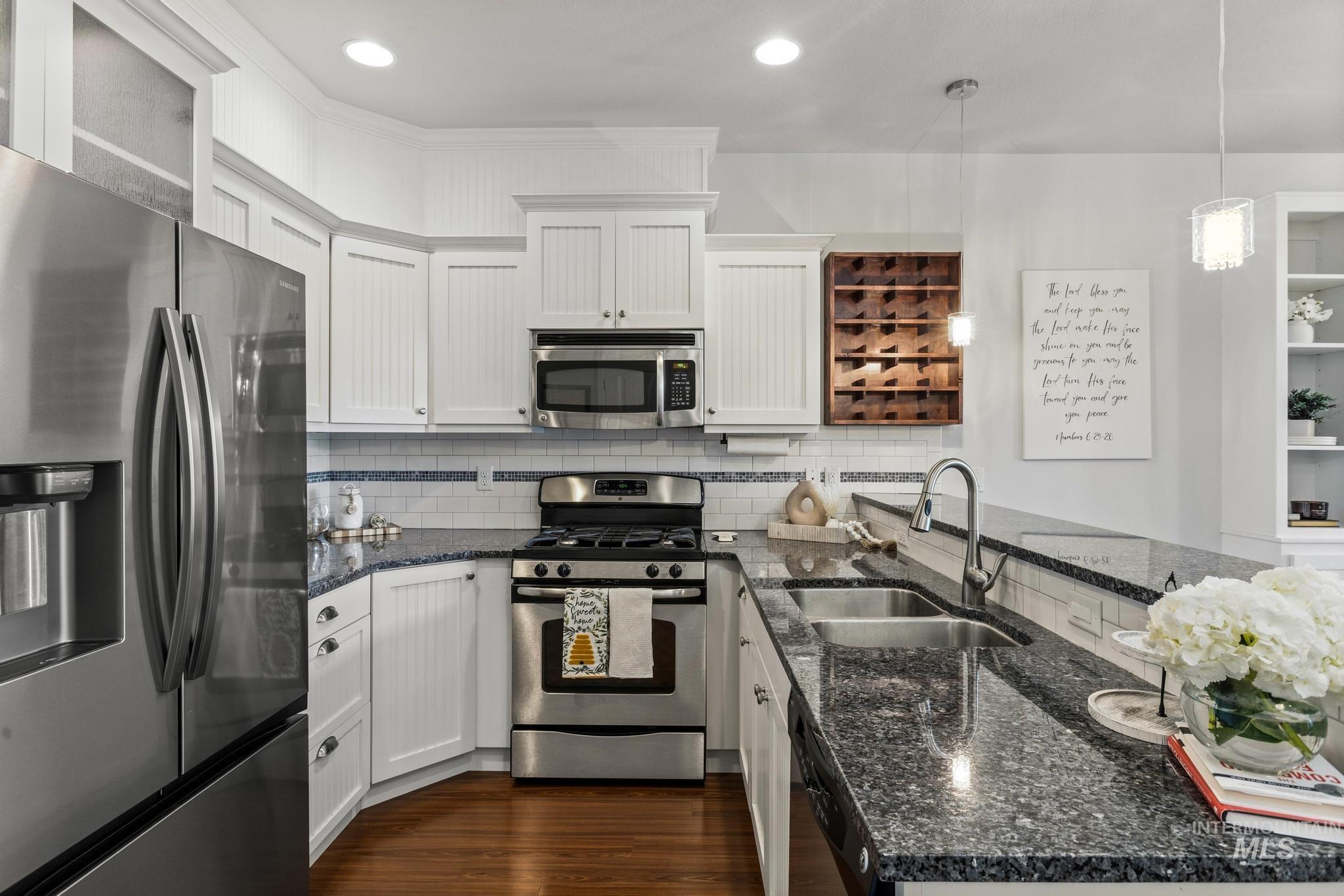 Kitchen featuring stainless steel appliances, dark stone counters, dark wood finished floors, decorative light fixtures, and white cabinets