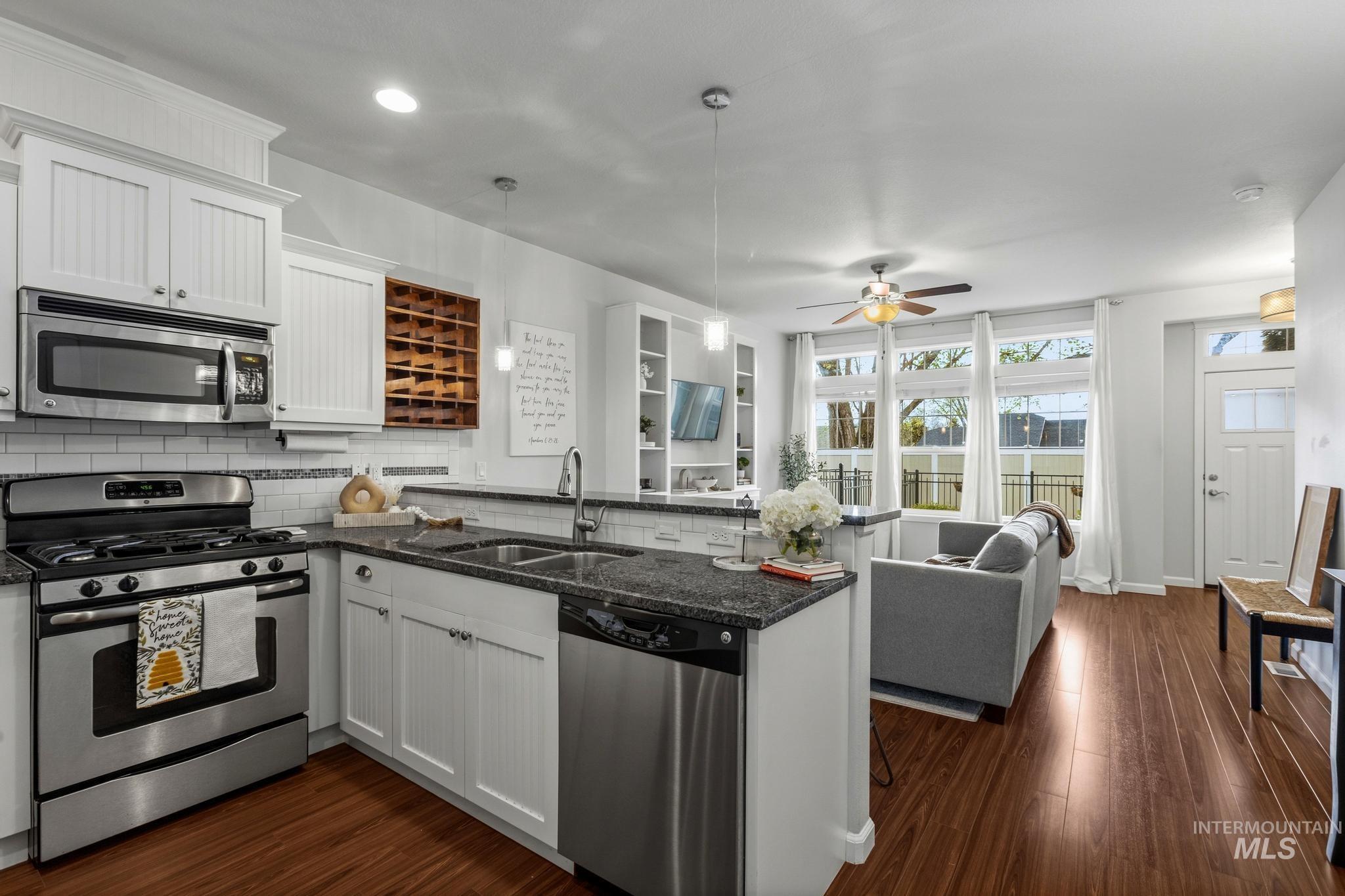 Kitchen with a peninsula, stainless steel appliances, white cabinets, and dark wood-style flooring